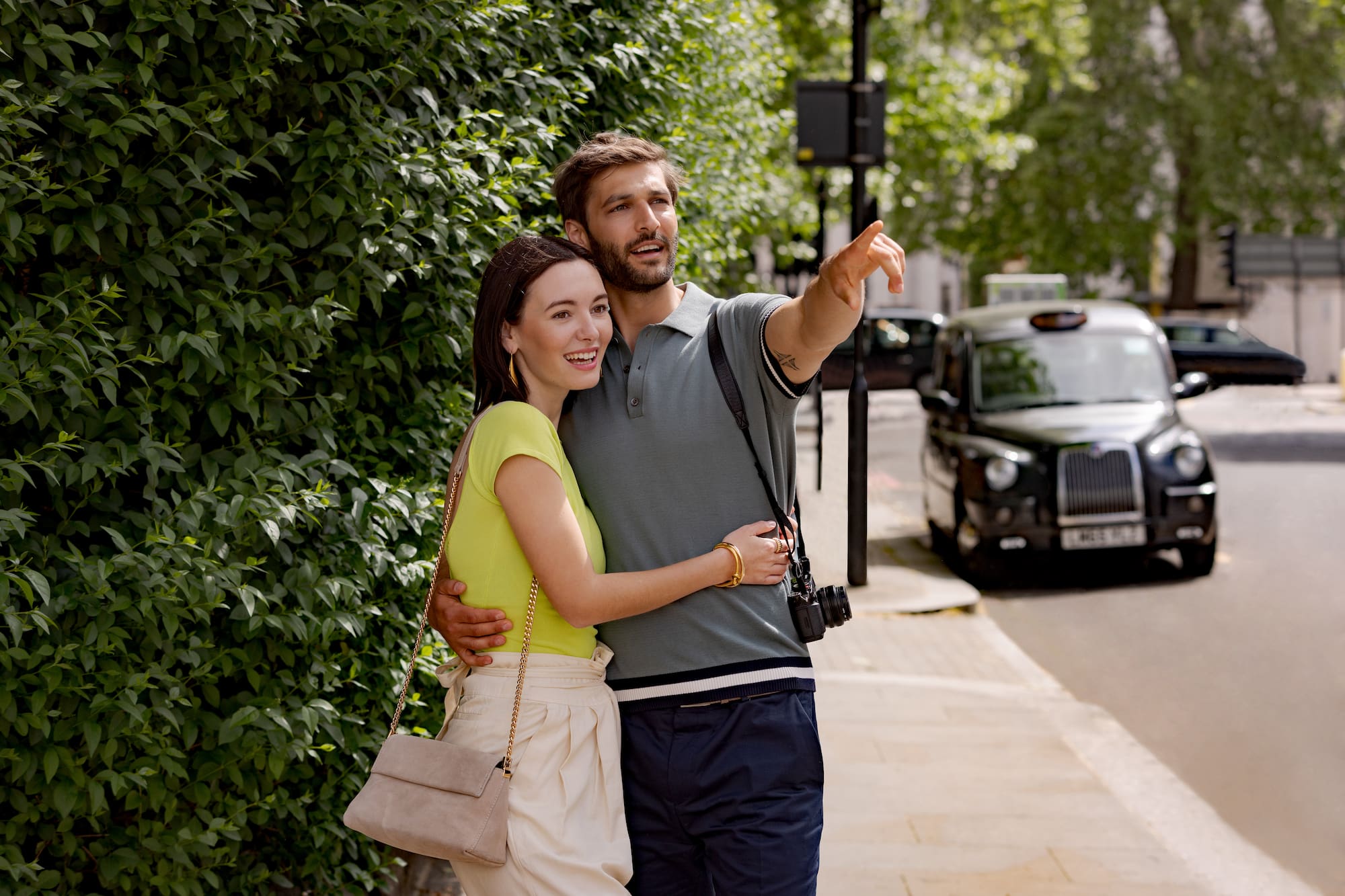 A man and a woman stand on the sidewalk, both pointing.