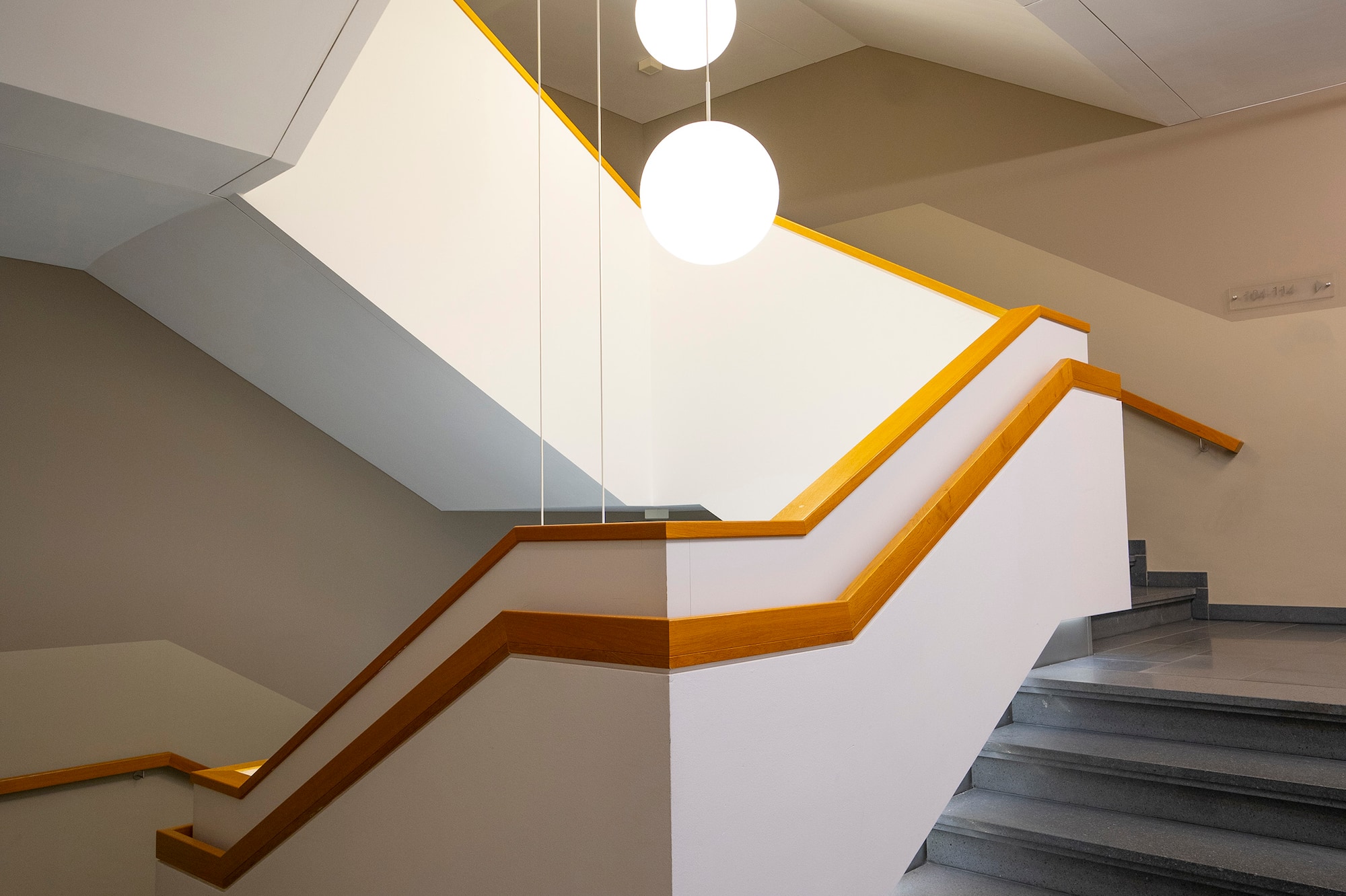Angular modern staircase, wooden handrails, spherical pendant lights.