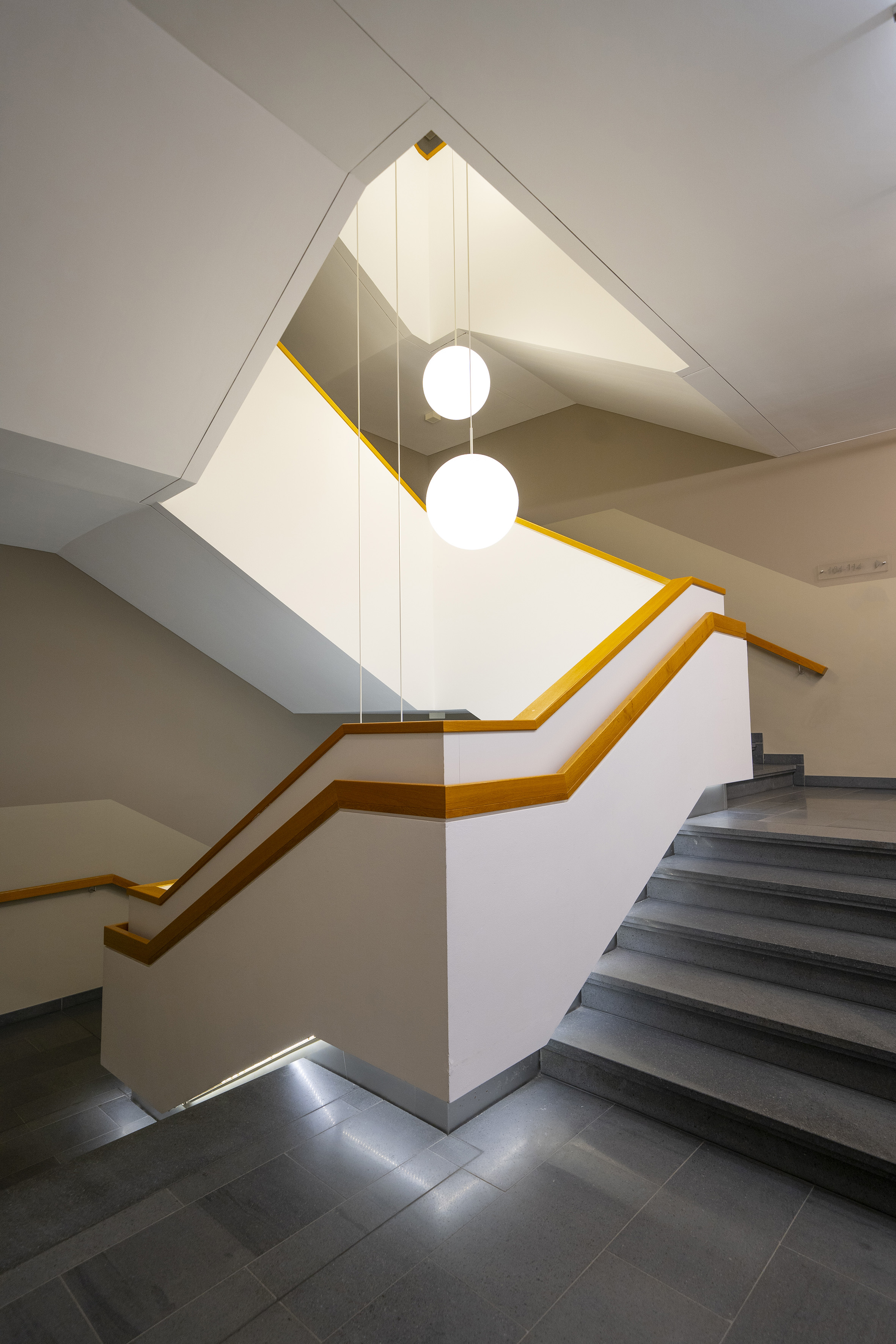Angular modern staircase, wooden handrails, spherical pendant lights.