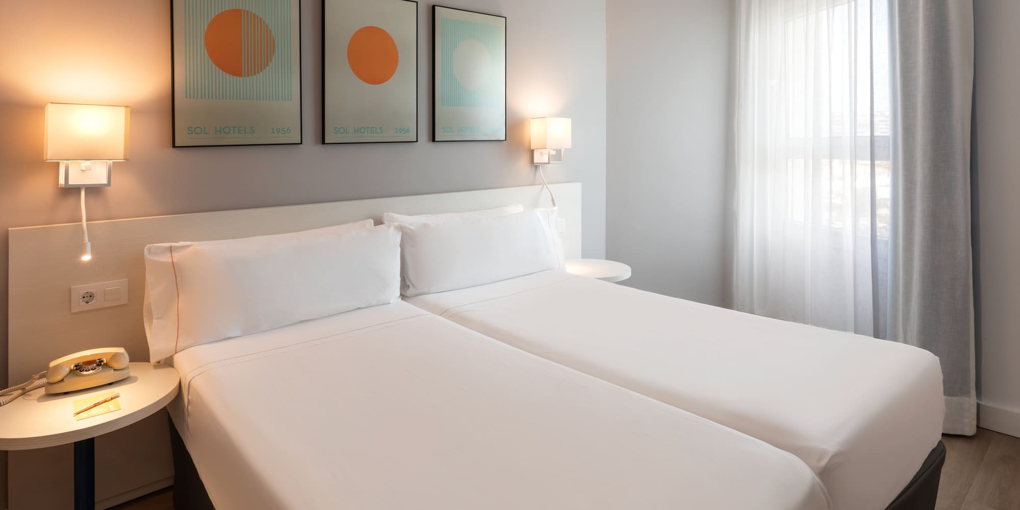 Clean modern hotel room with twin beds, white bedding, and abstract art.