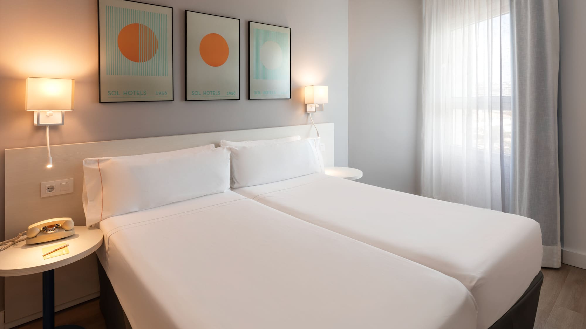 Clean modern hotel room with twin beds, white bedding, and abstract art.