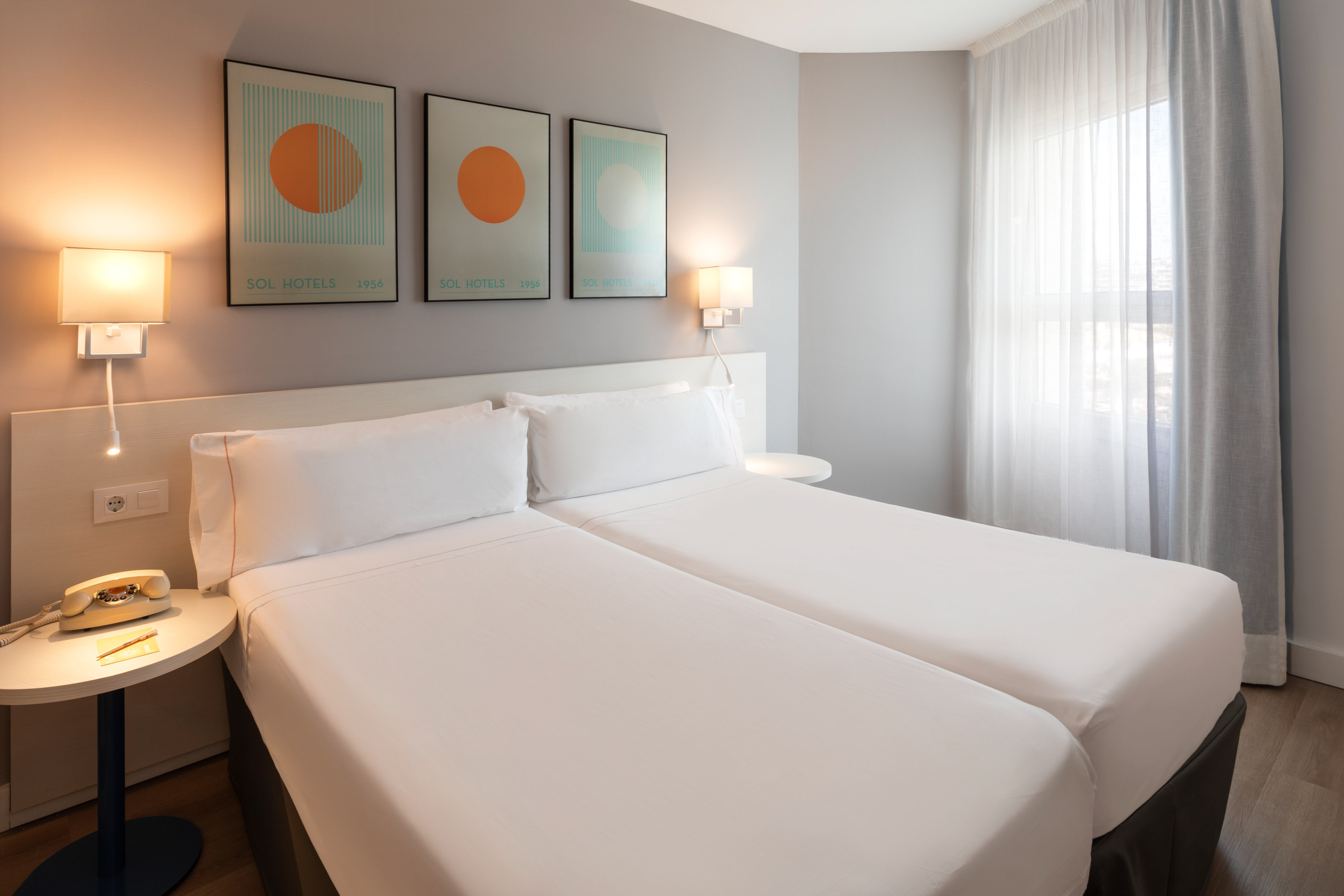 Sol Hotels twin bedroom with clean white beds, modern art, and bedside lighting.