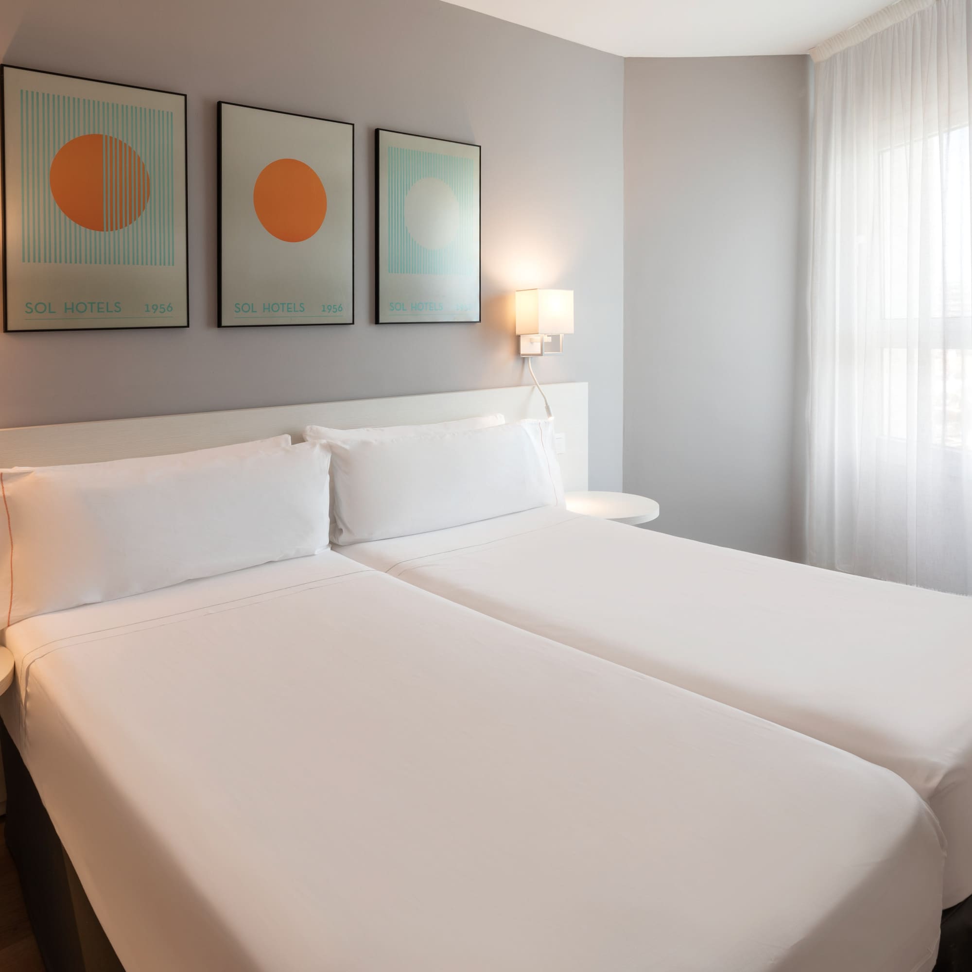 Clean modern hotel room with twin beds, white bedding, and abstract art.