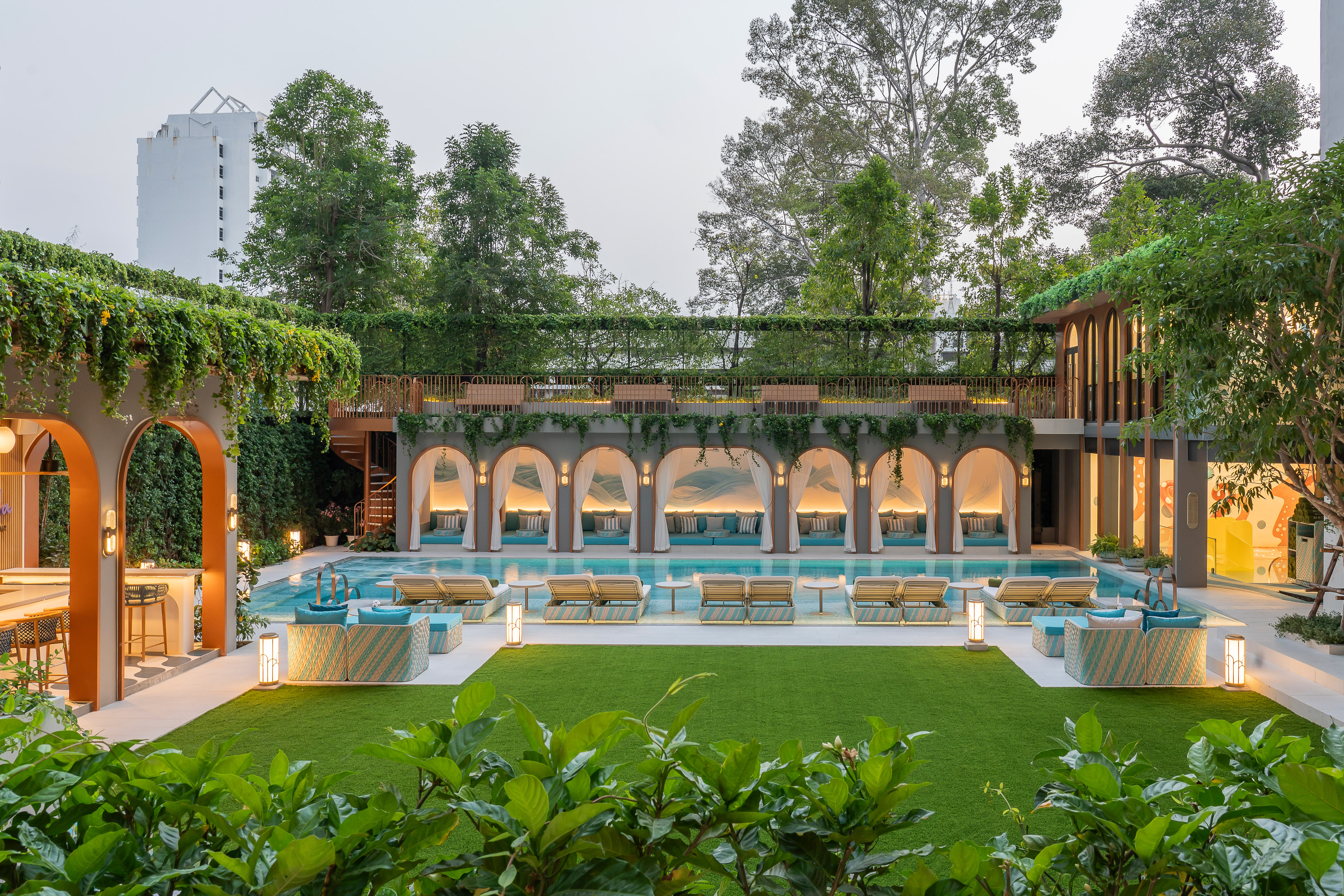 Elegant hotel pool with arched cabanas, daybeds, and landscaped green space.