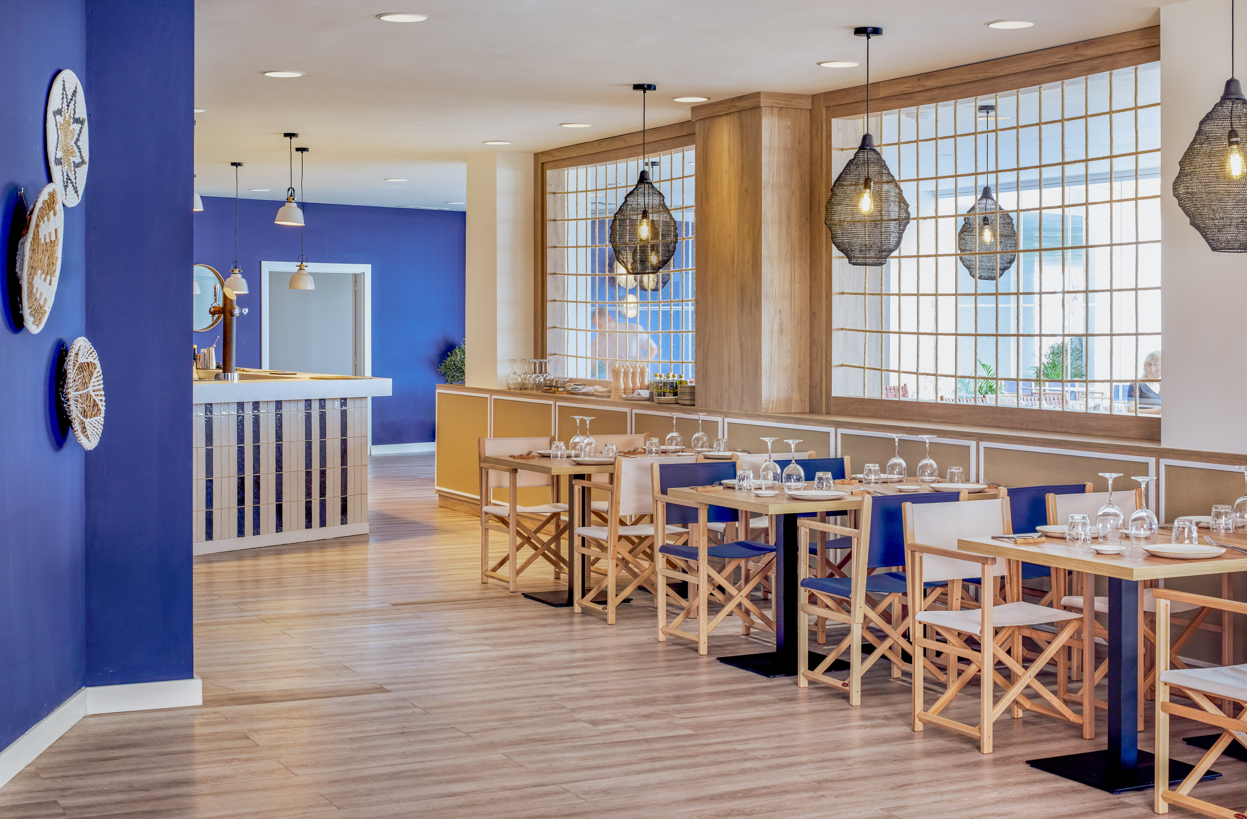 Blue-walled restaurant dining area with wooden tables and woven pendant lights.