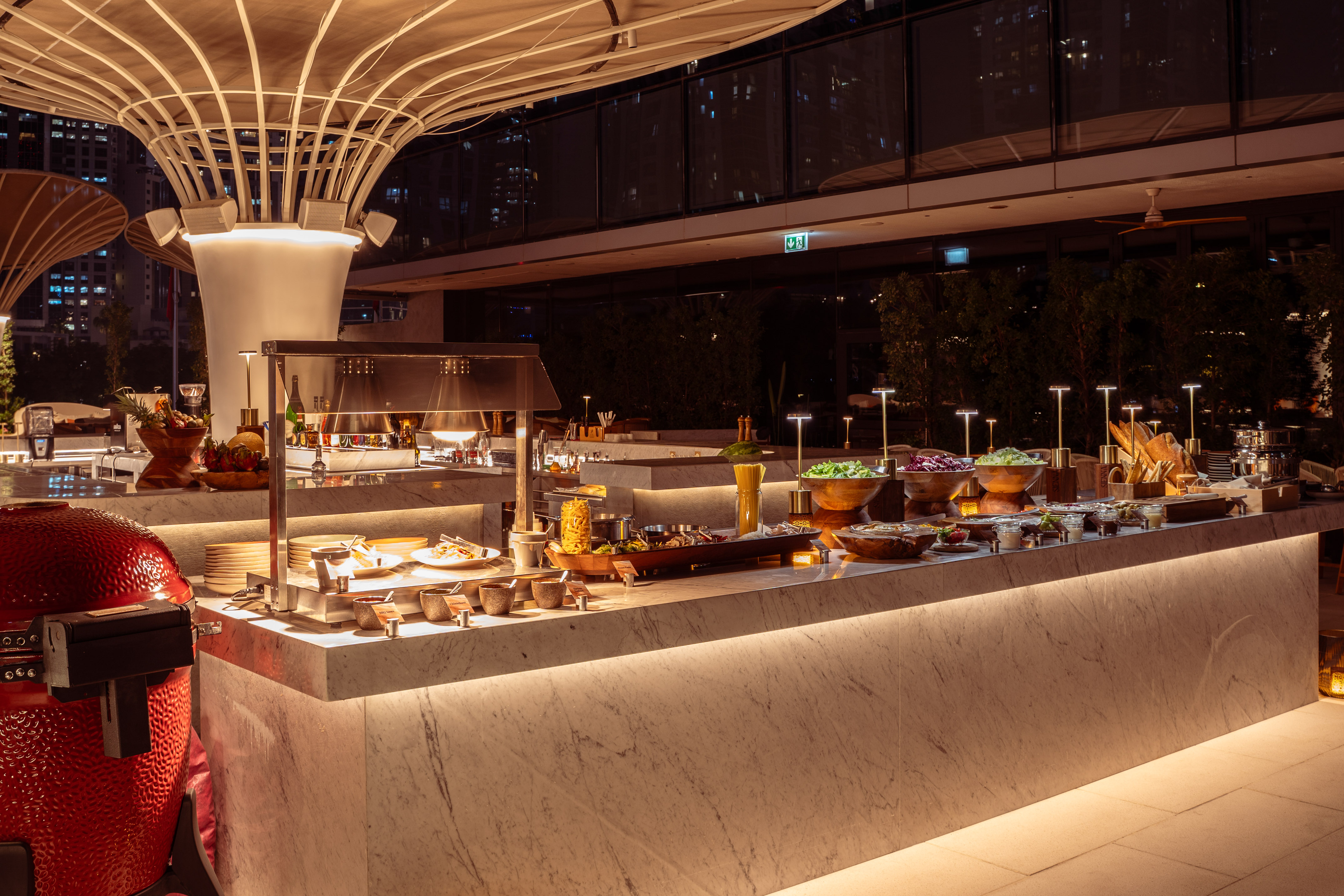 Night outdoor buffet with marble food counter, modern lighting, and fresh dishes.