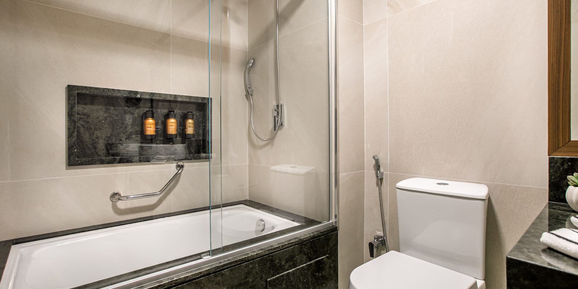 Modern tiled bathroom with bathtub, shower, toilet, and stone vanity.