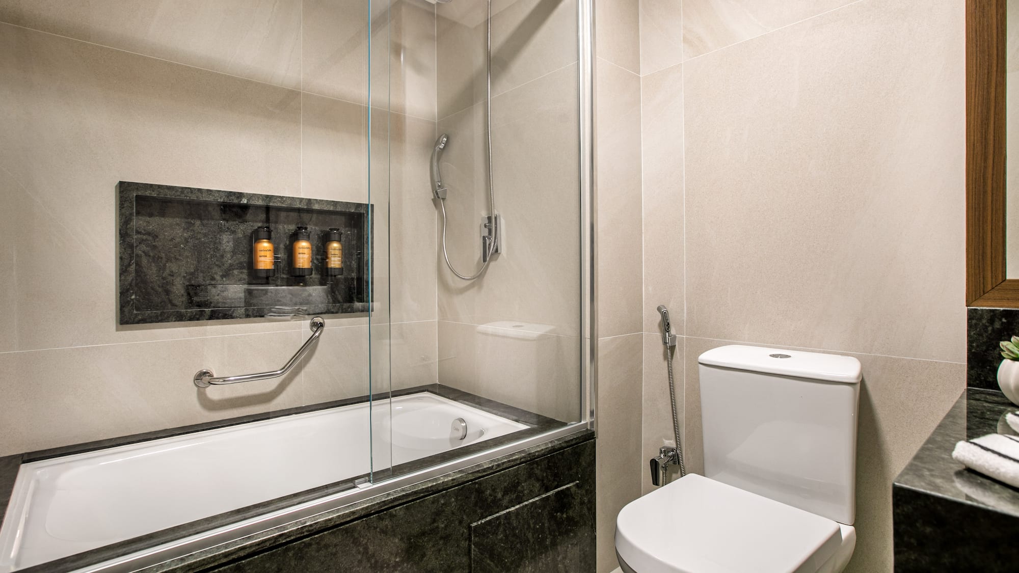 Modern tiled bathroom with bathtub, shower, toilet, and stone vanity.