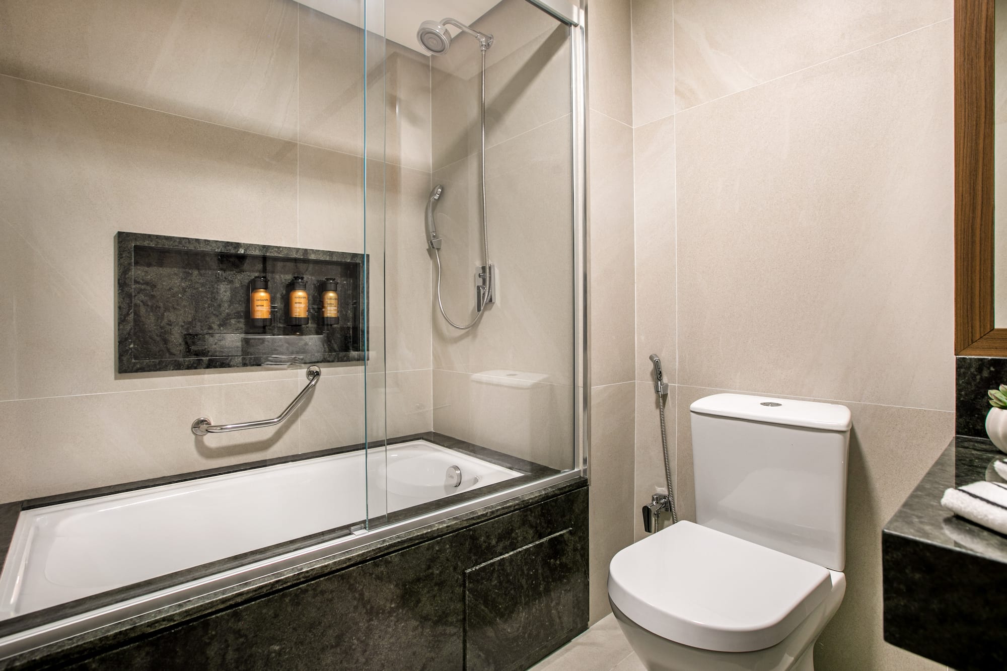Modern tiled bathroom with bathtub, shower, toilet, and stone vanity.