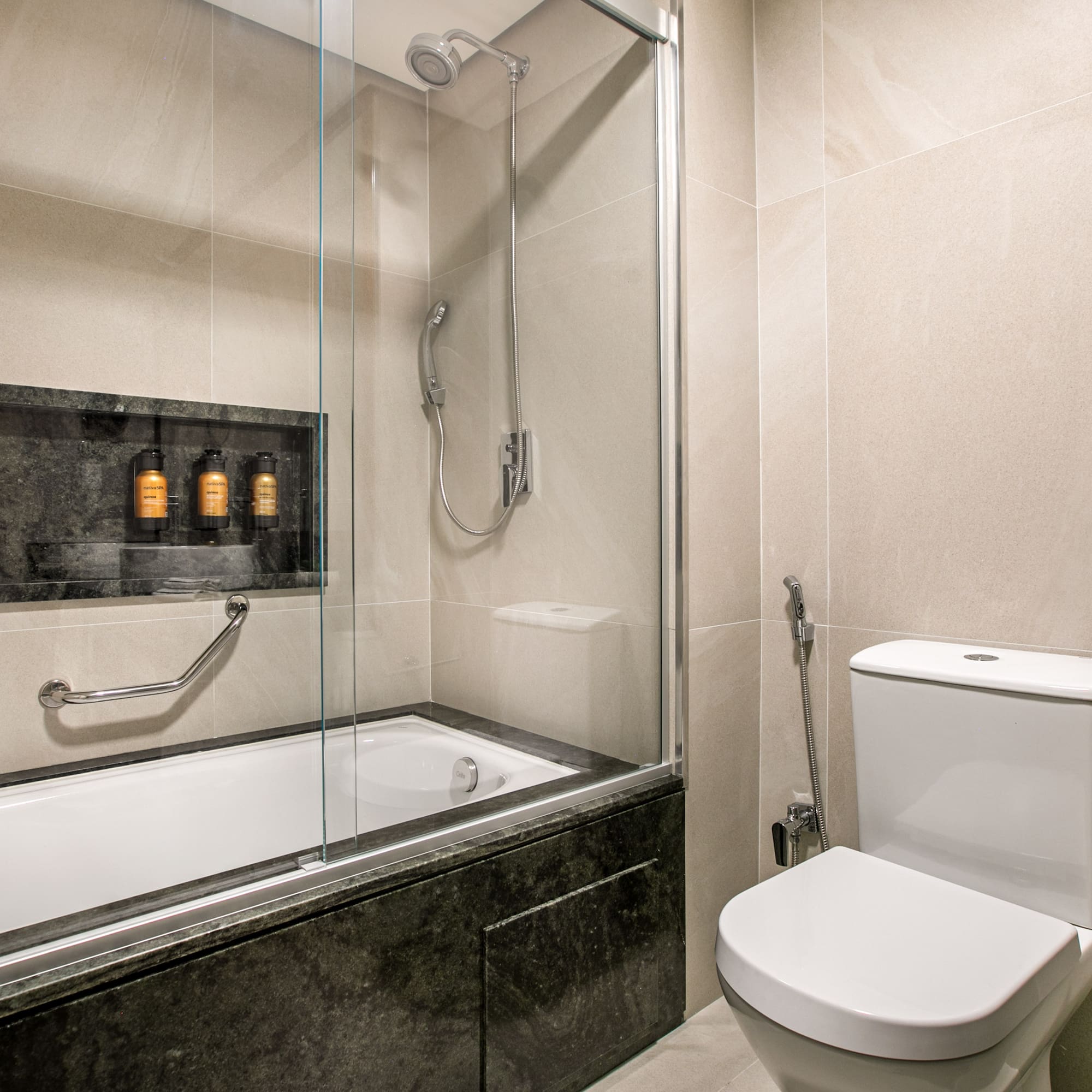 Modern tiled bathroom with bathtub, shower, toilet, and stone vanity.