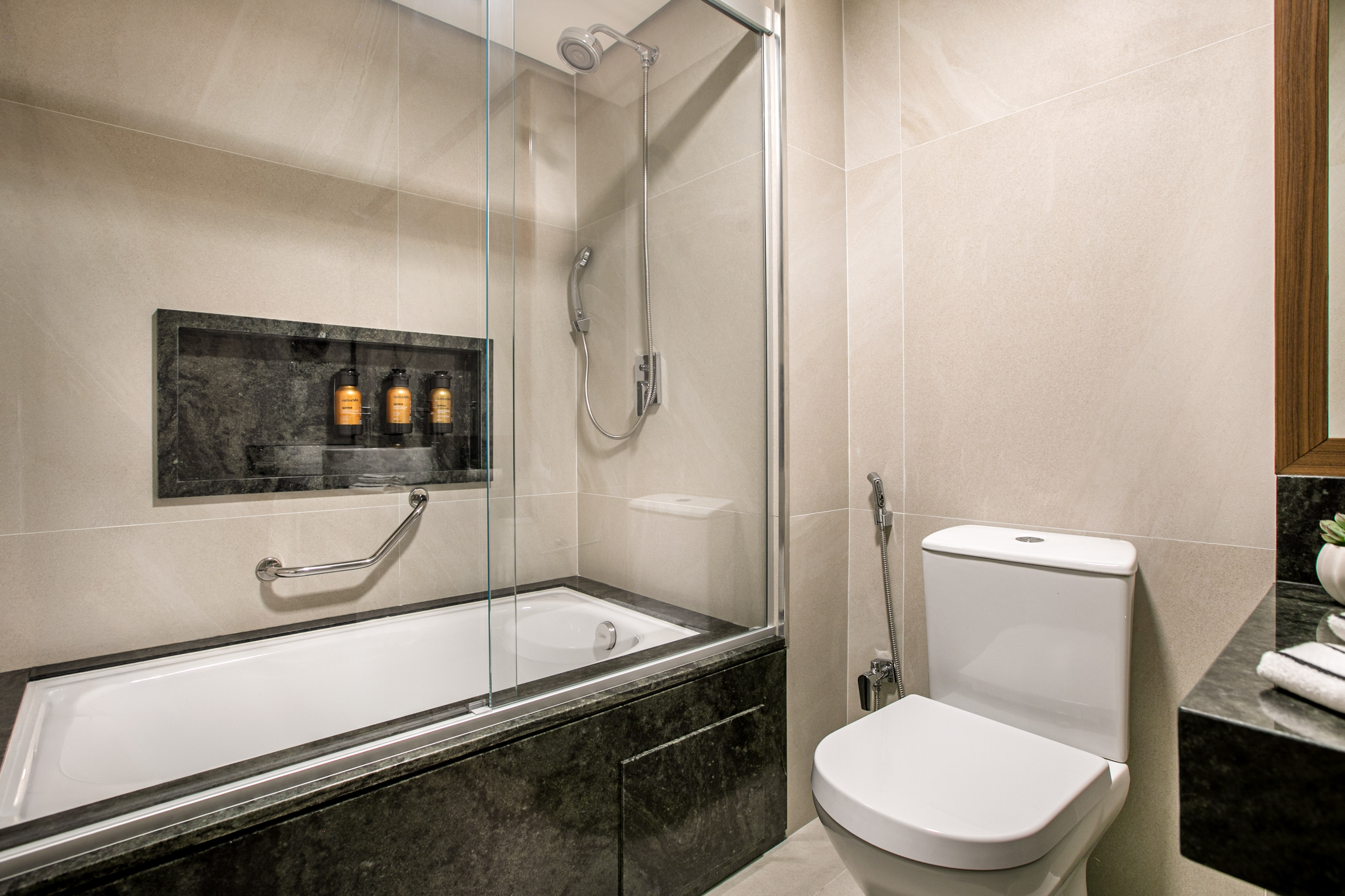 Modern tiled bathroom with bathtub, shower, toilet, and stone vanity.