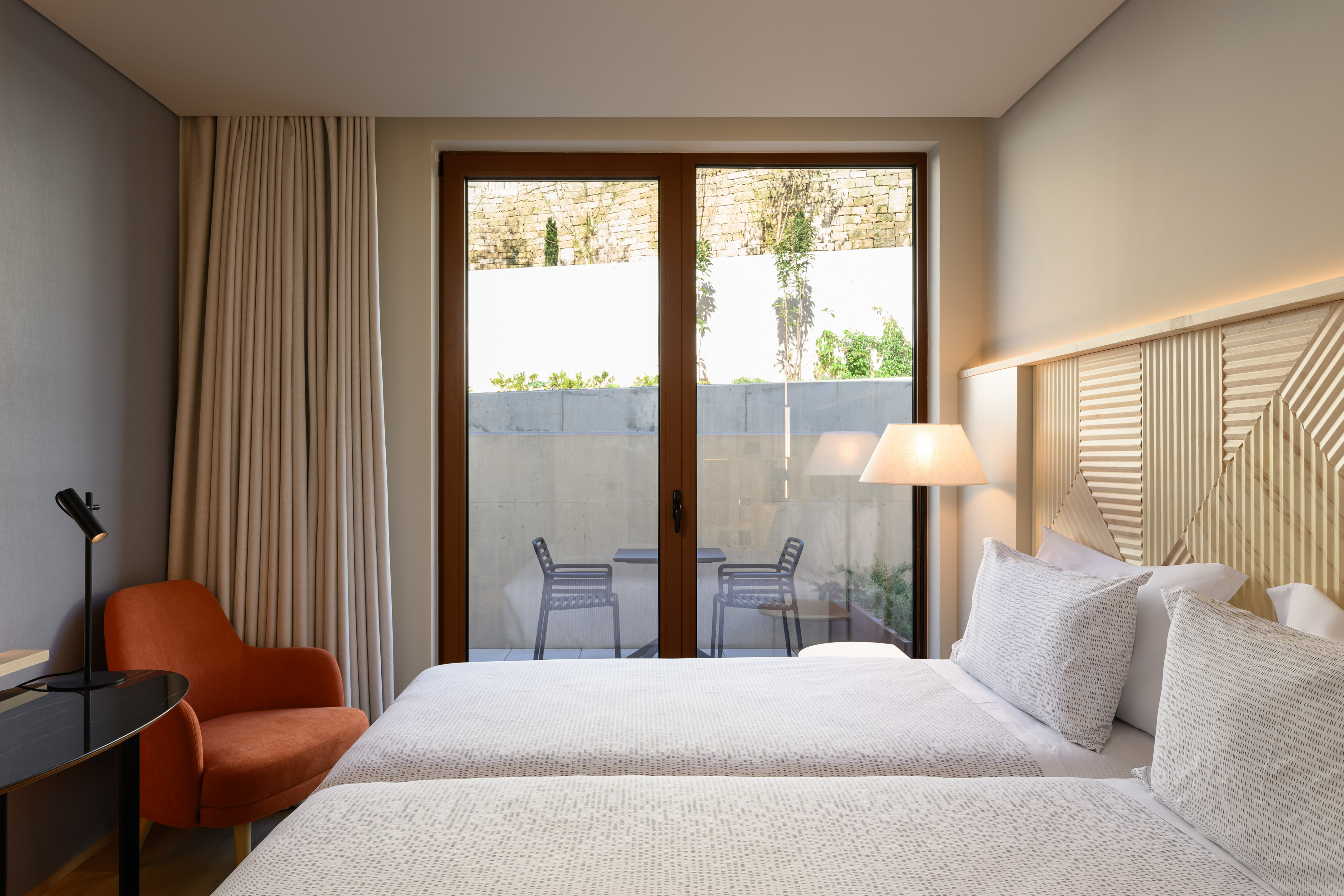 Contemporary hotel bedroom with twin beds, patterned headboard, and private terrace.