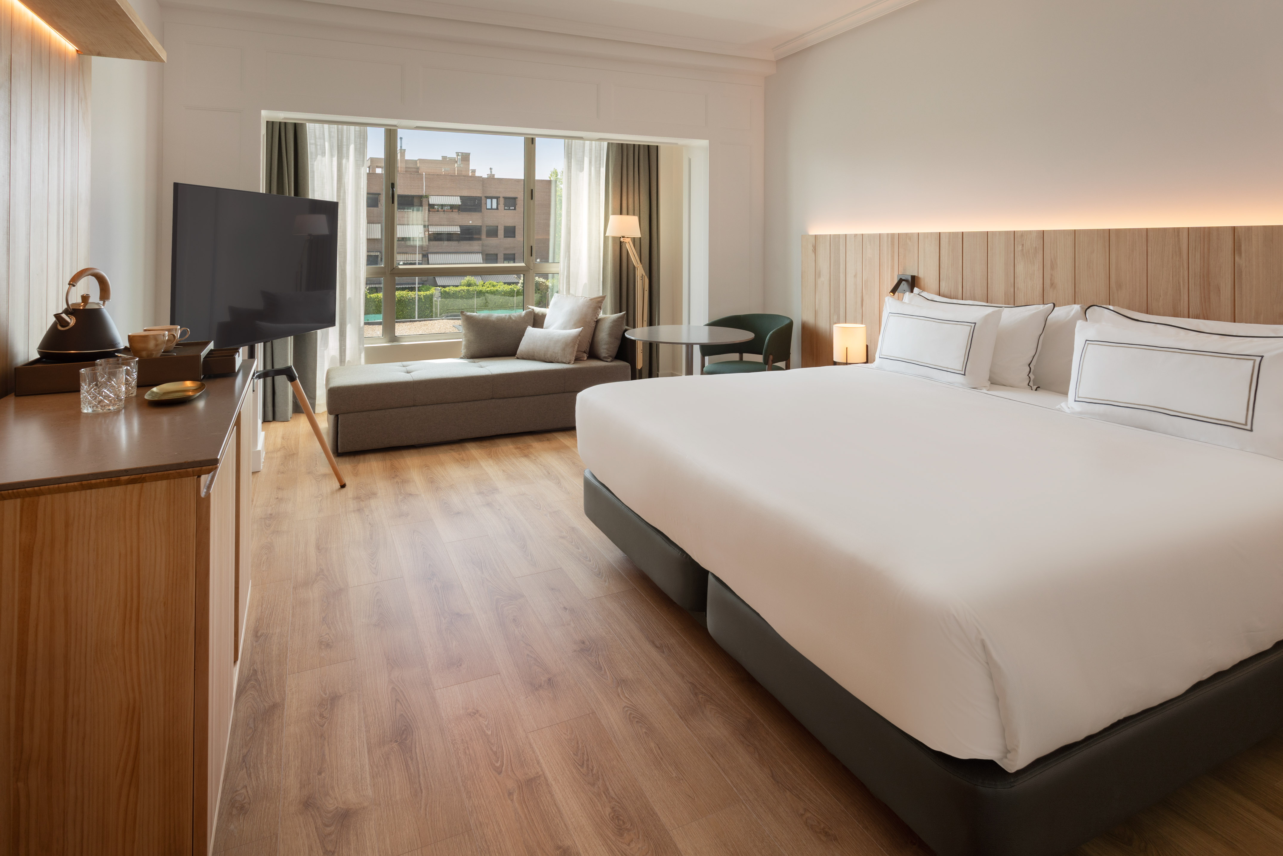 Bright hotel room with large bed, window daybed, wood floor, and television.