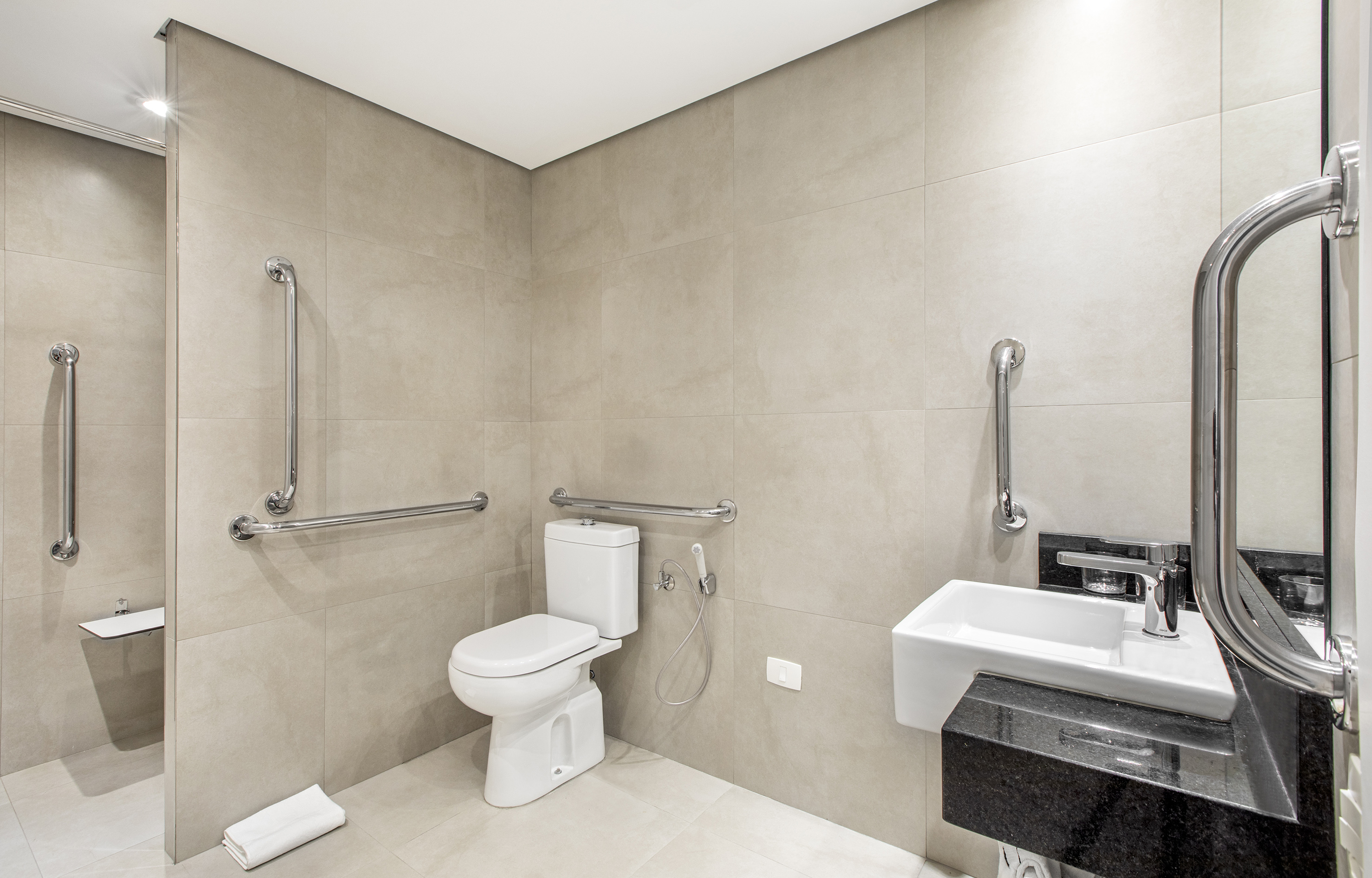 Beige accessible bathroom with toilet, sink, grab bars, and shower seat.