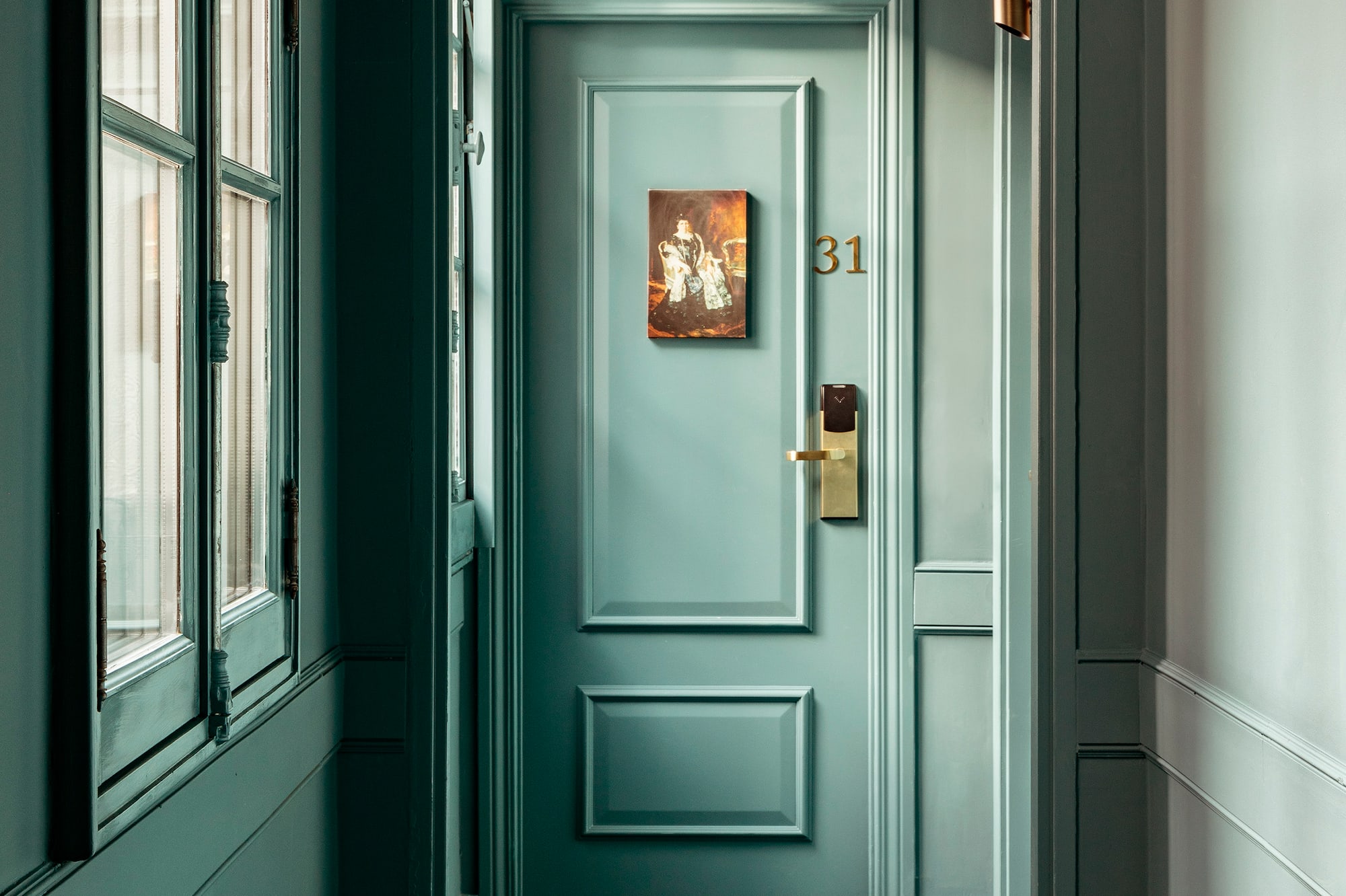 Teal hotel hallway leading to room 31 with vintage painting and gold handle.