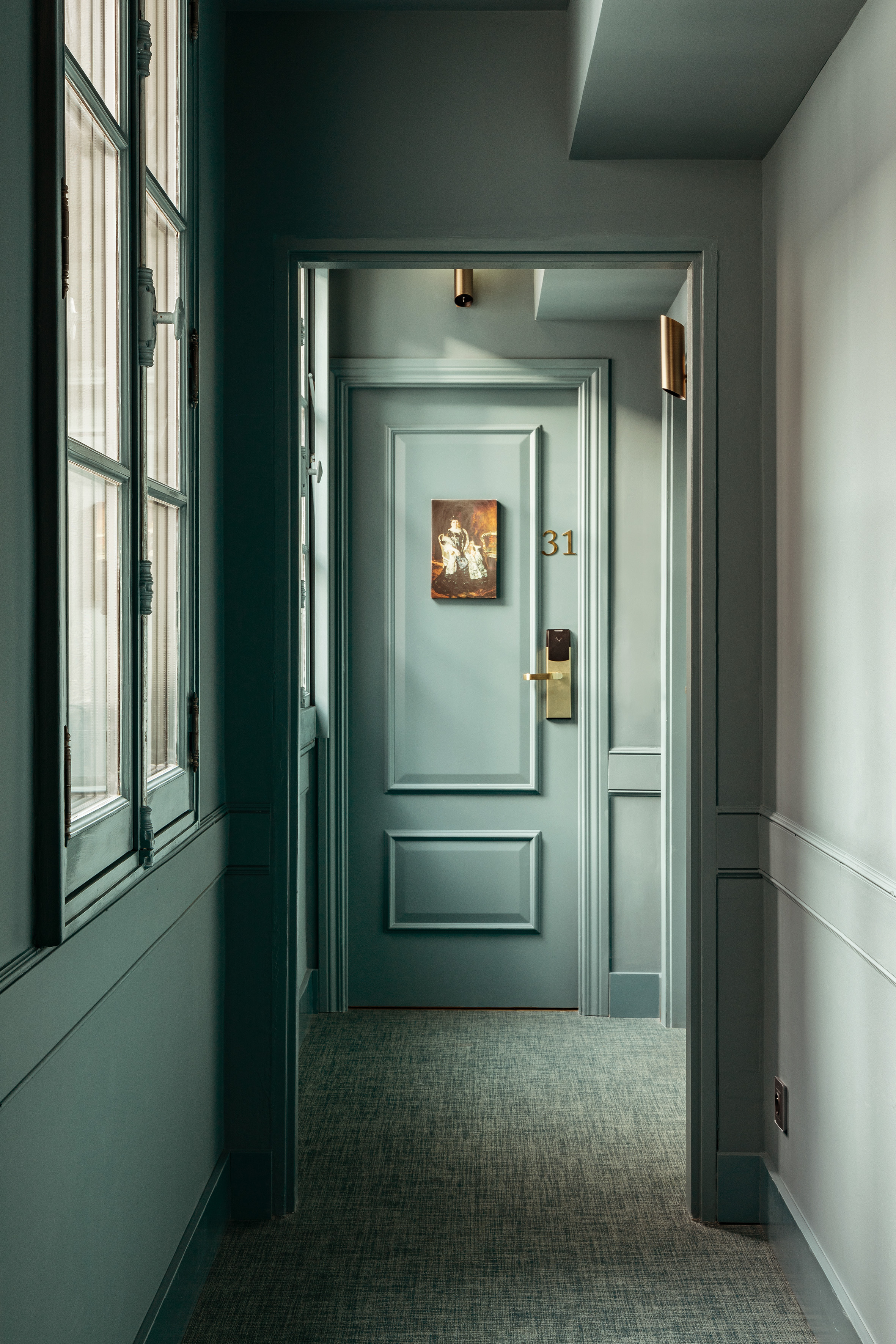 Teal hotel hallway leading to room 31 with vintage painting and gold handle.