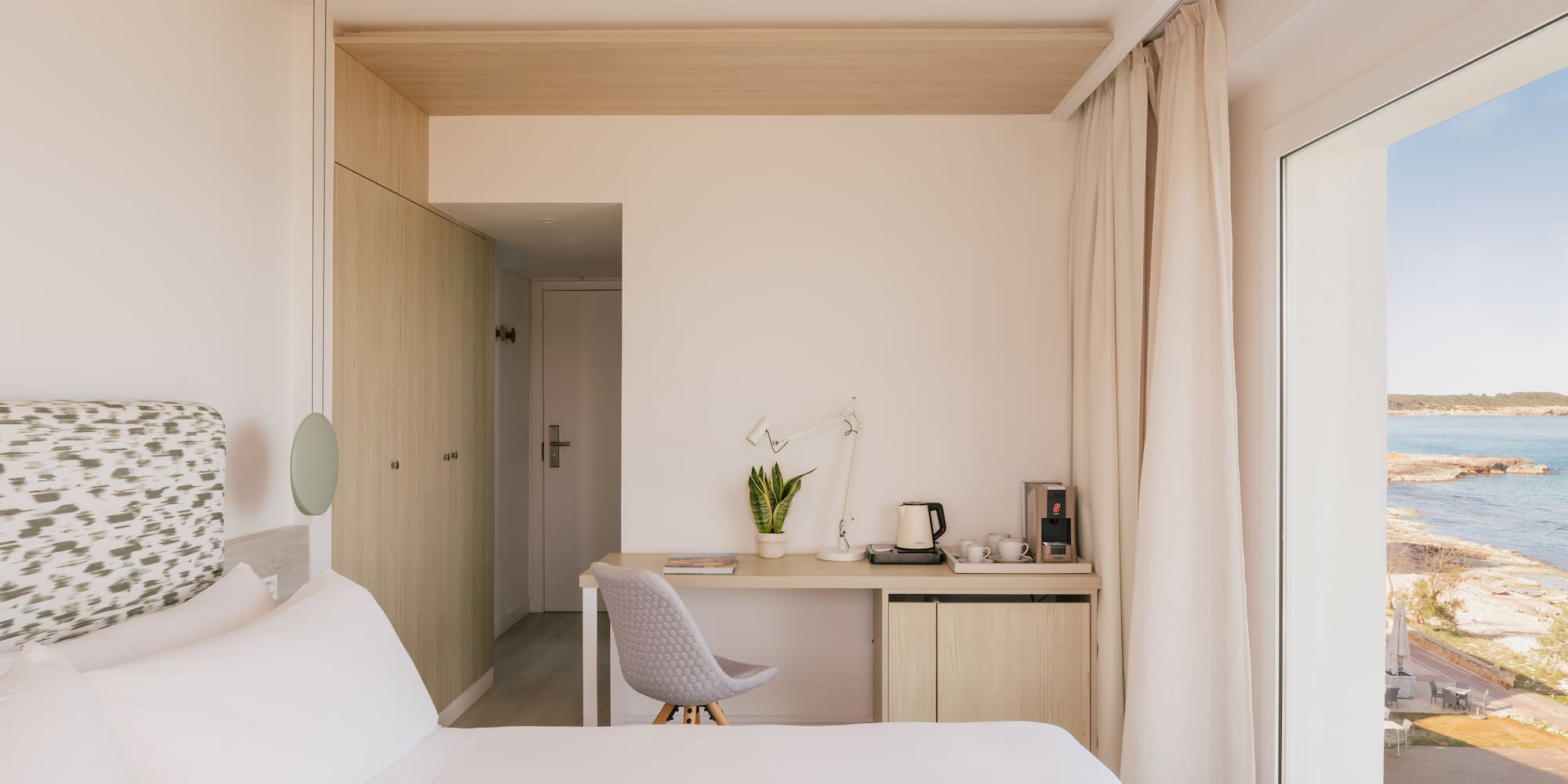 Modern hotel bedroom with sea view, desk, and coffee station.