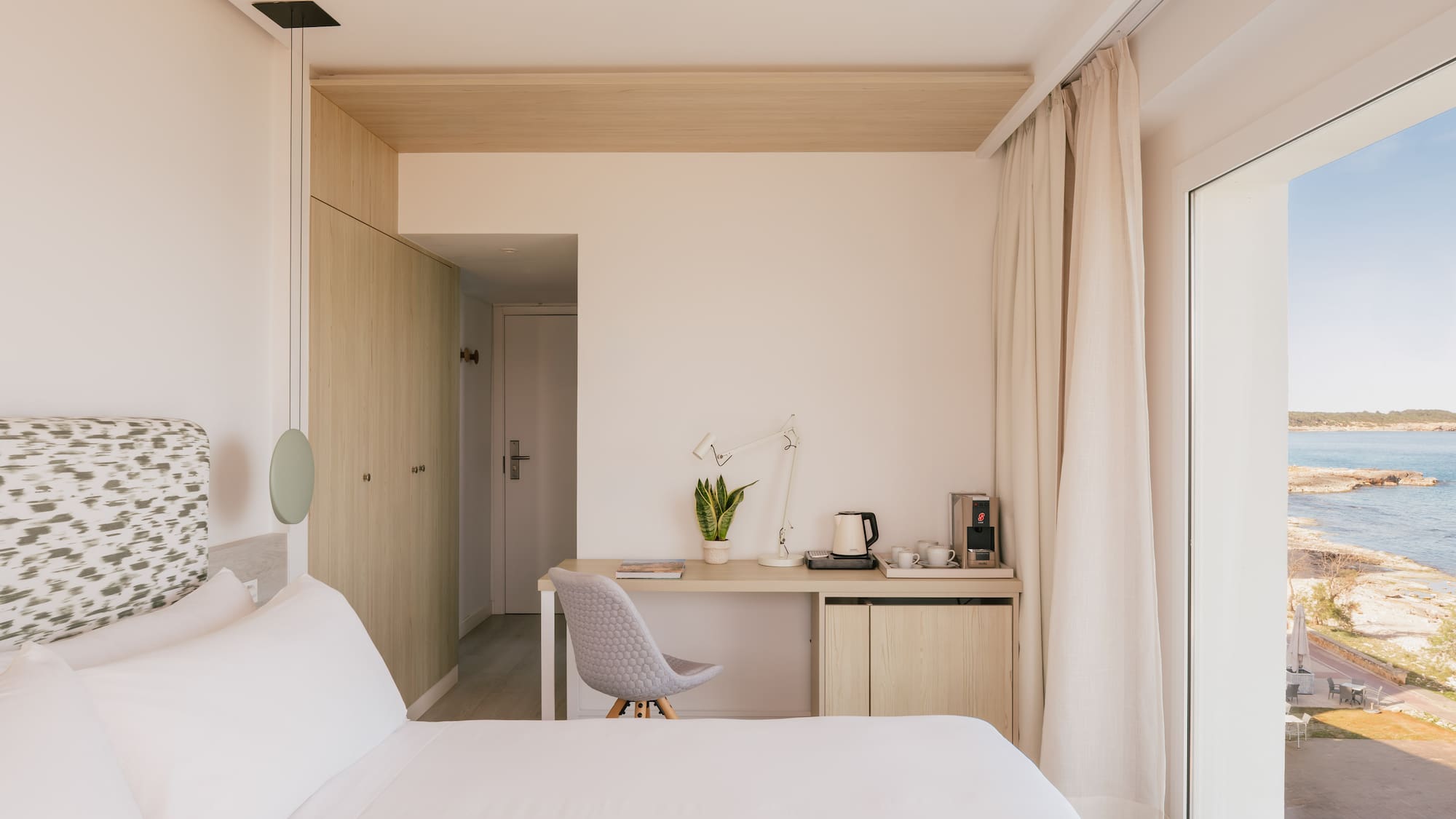 Modern hotel bedroom with sea view, desk, and coffee station.