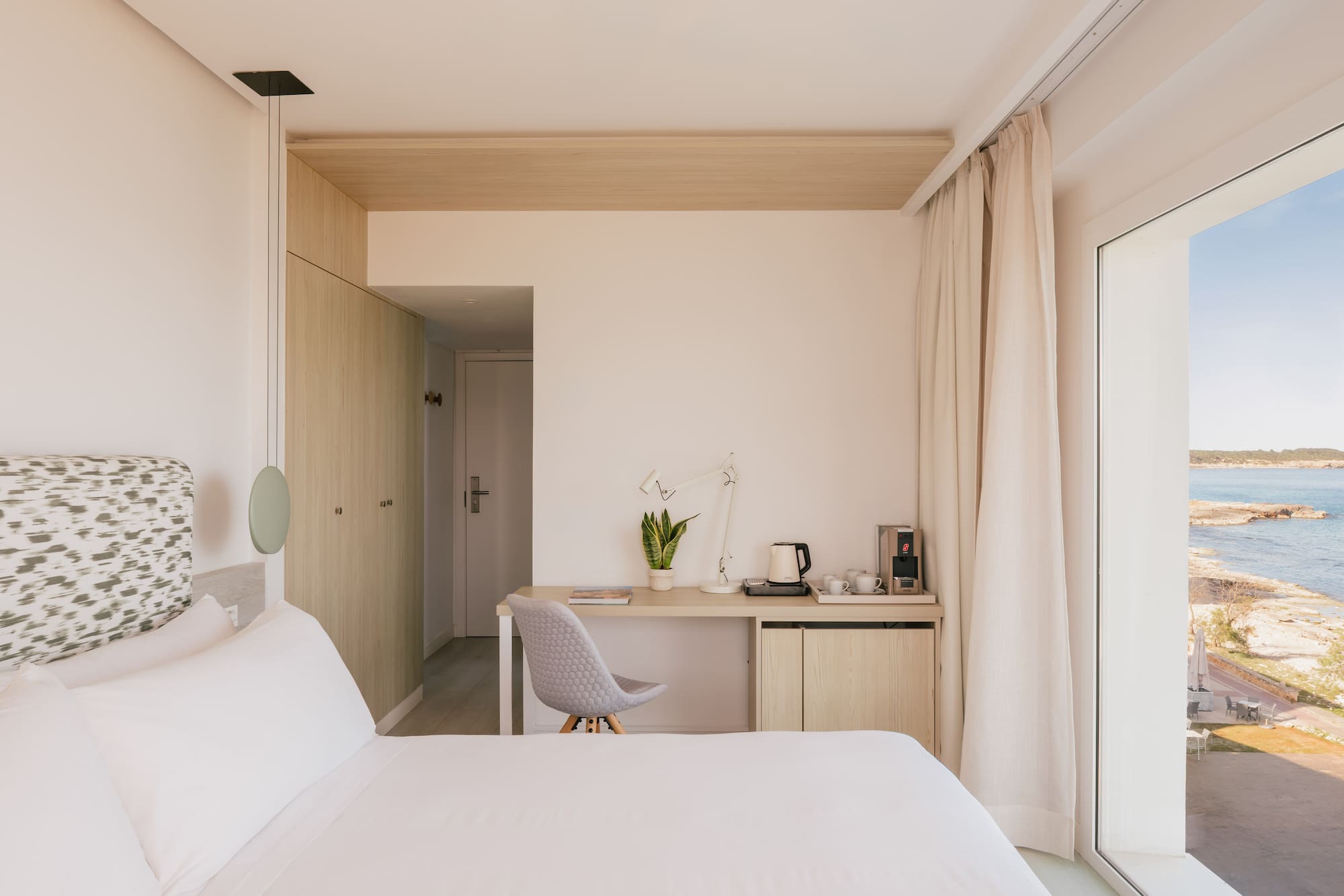 Habitación hotel moderna con escritorio, armario y vista al mar.