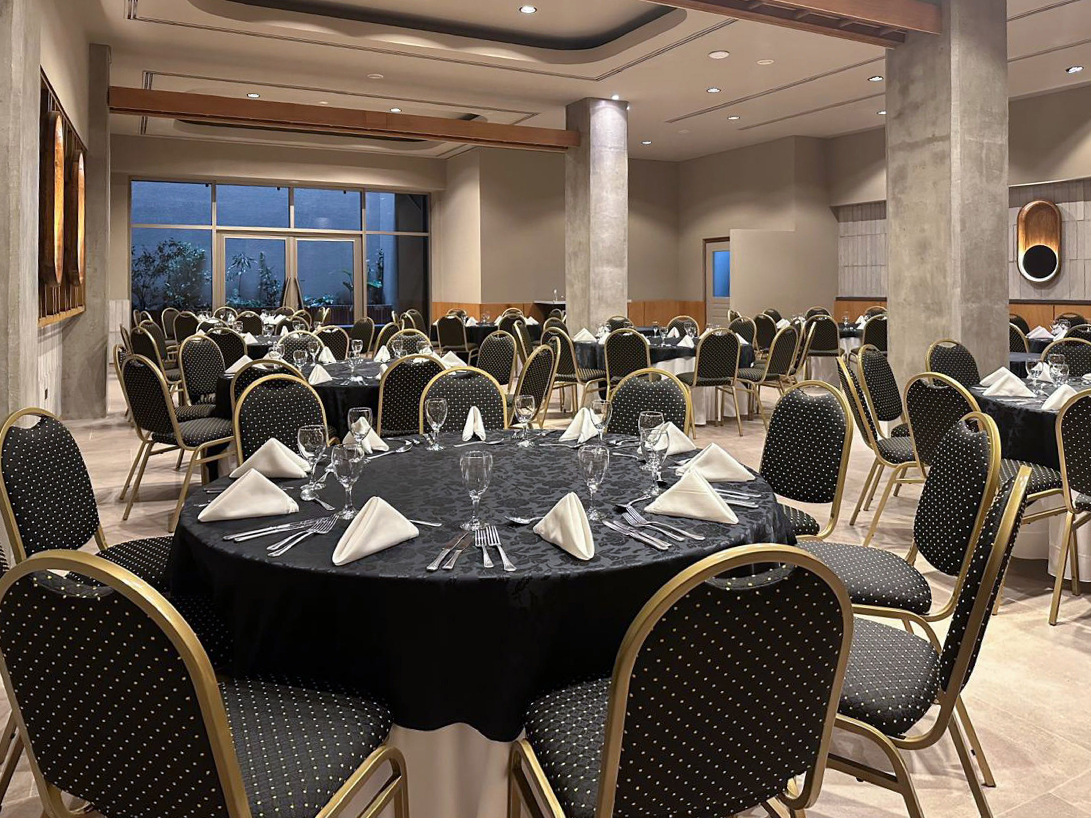 Spacious banquet room with round tables, black tablecloths, and gold-trimmed chairs.