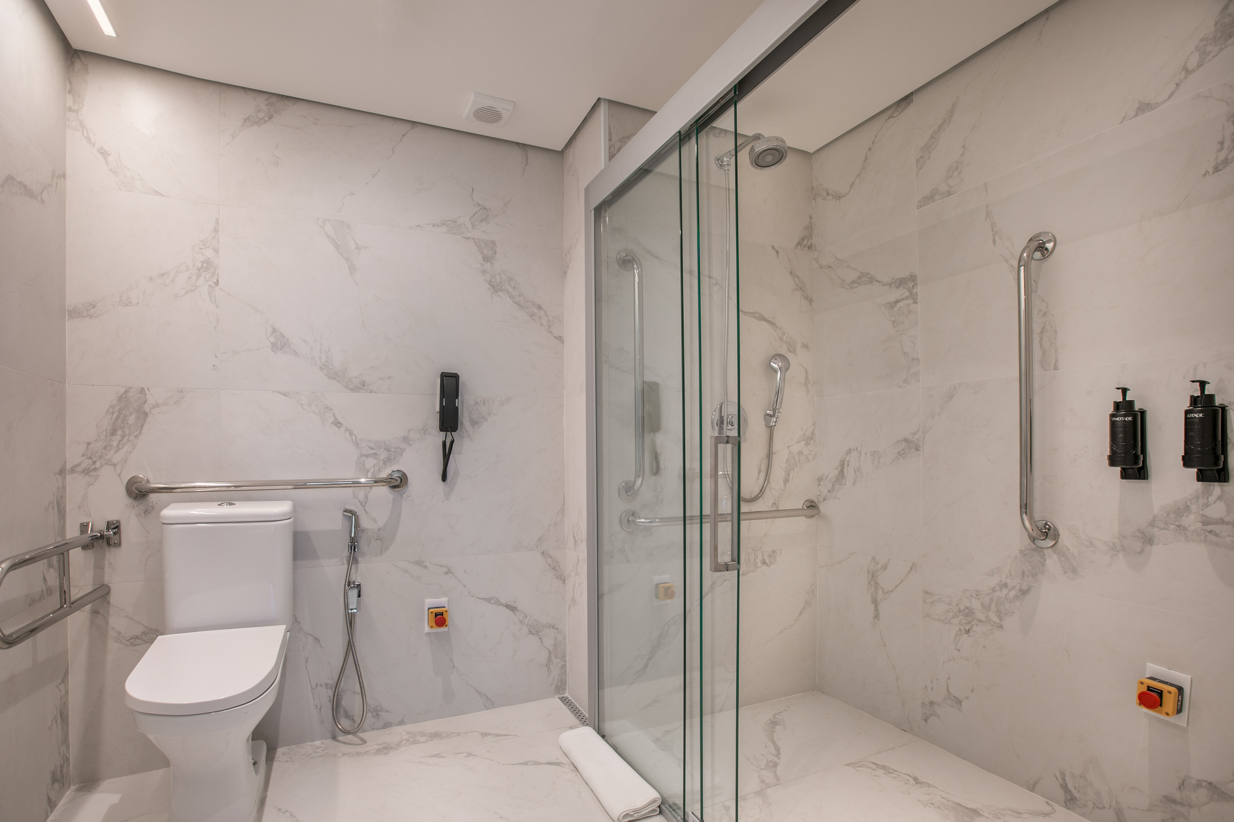 Accessible bathroom: white marble, toilet with grab bars, glass walk-in shower.