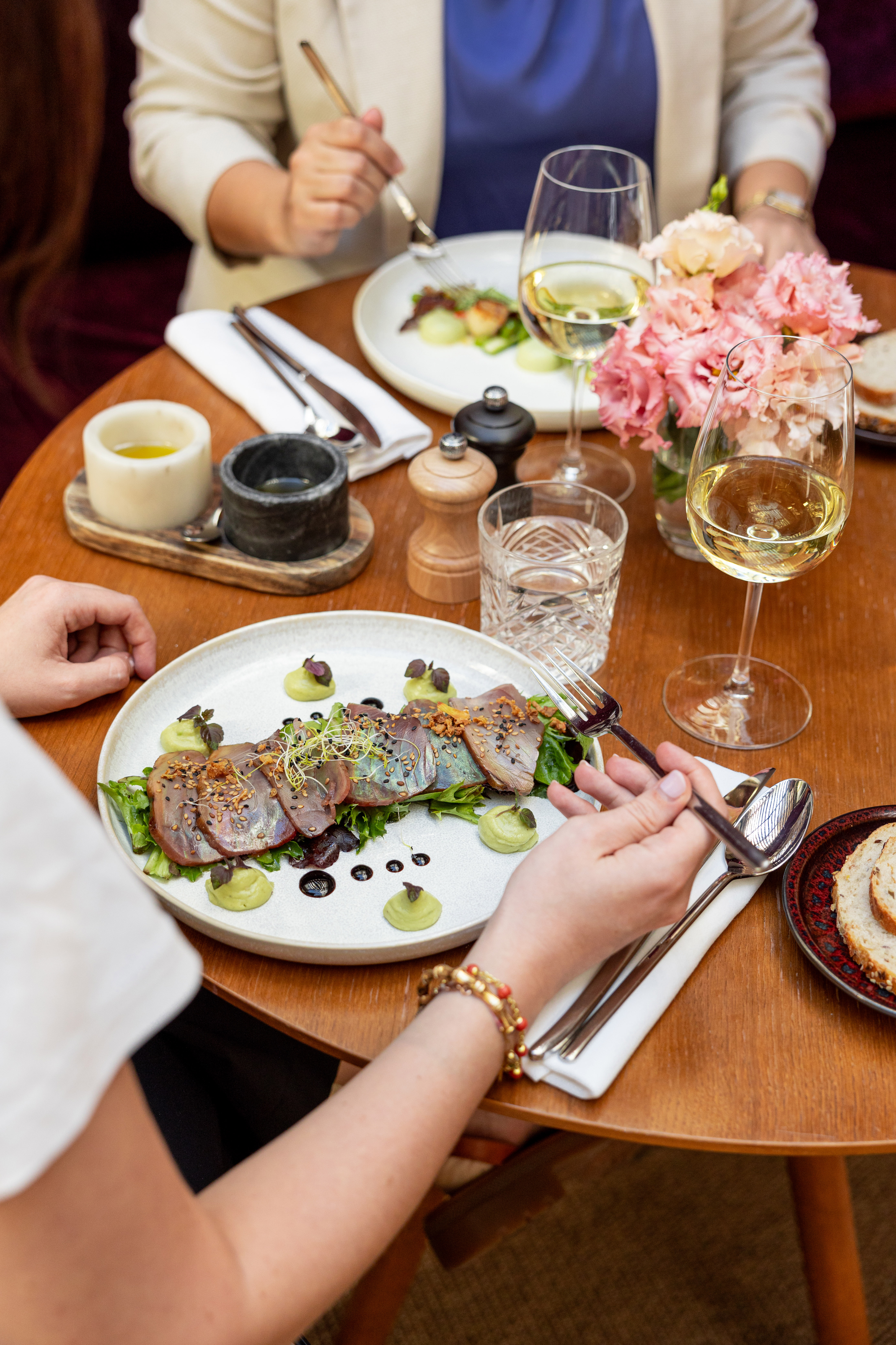 Seared tuna tataki, white wine, and flowers on an elegant dining table.