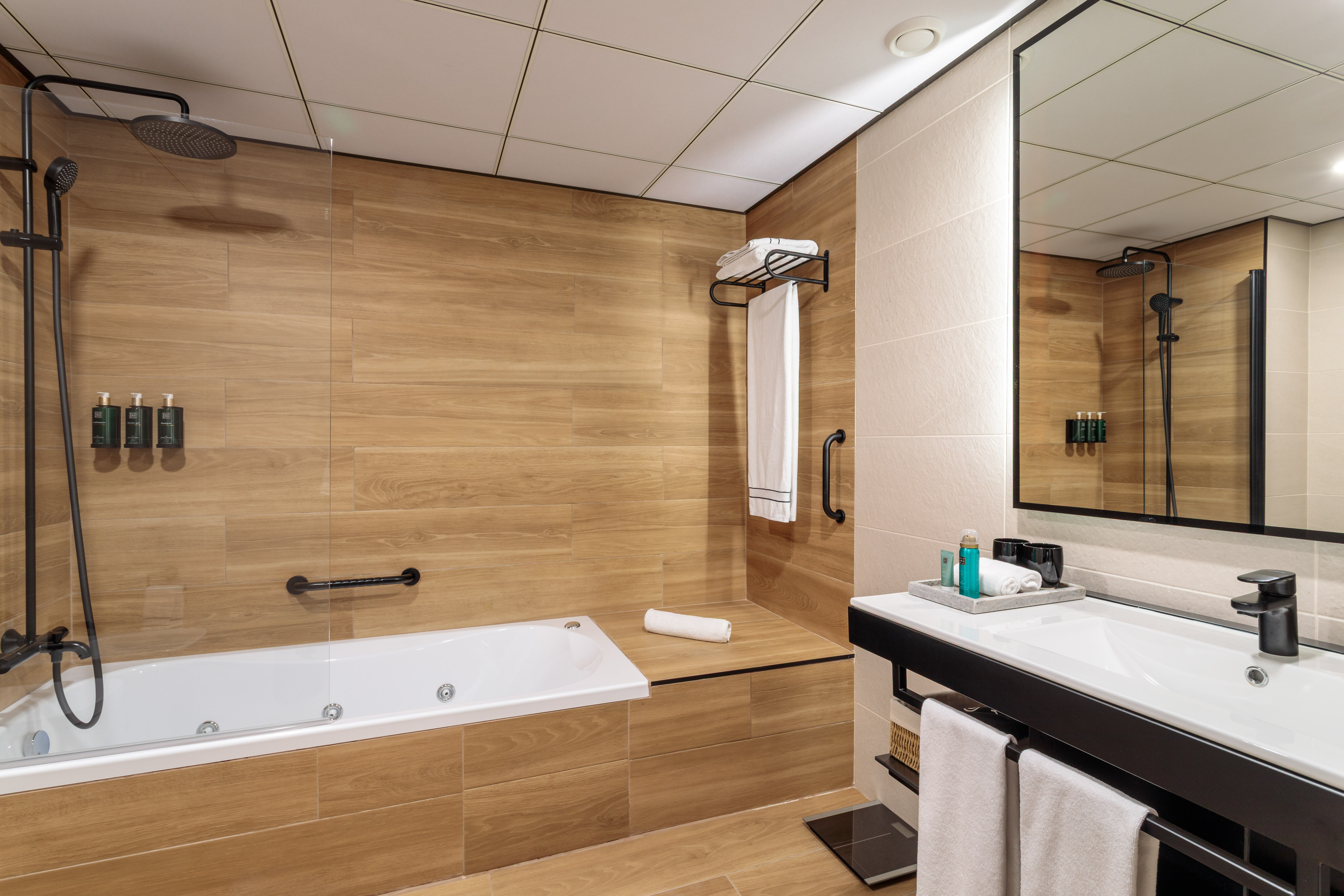 Baño moderno con bañera de hidromasaje, ducha de lluvia y lavabo negro.