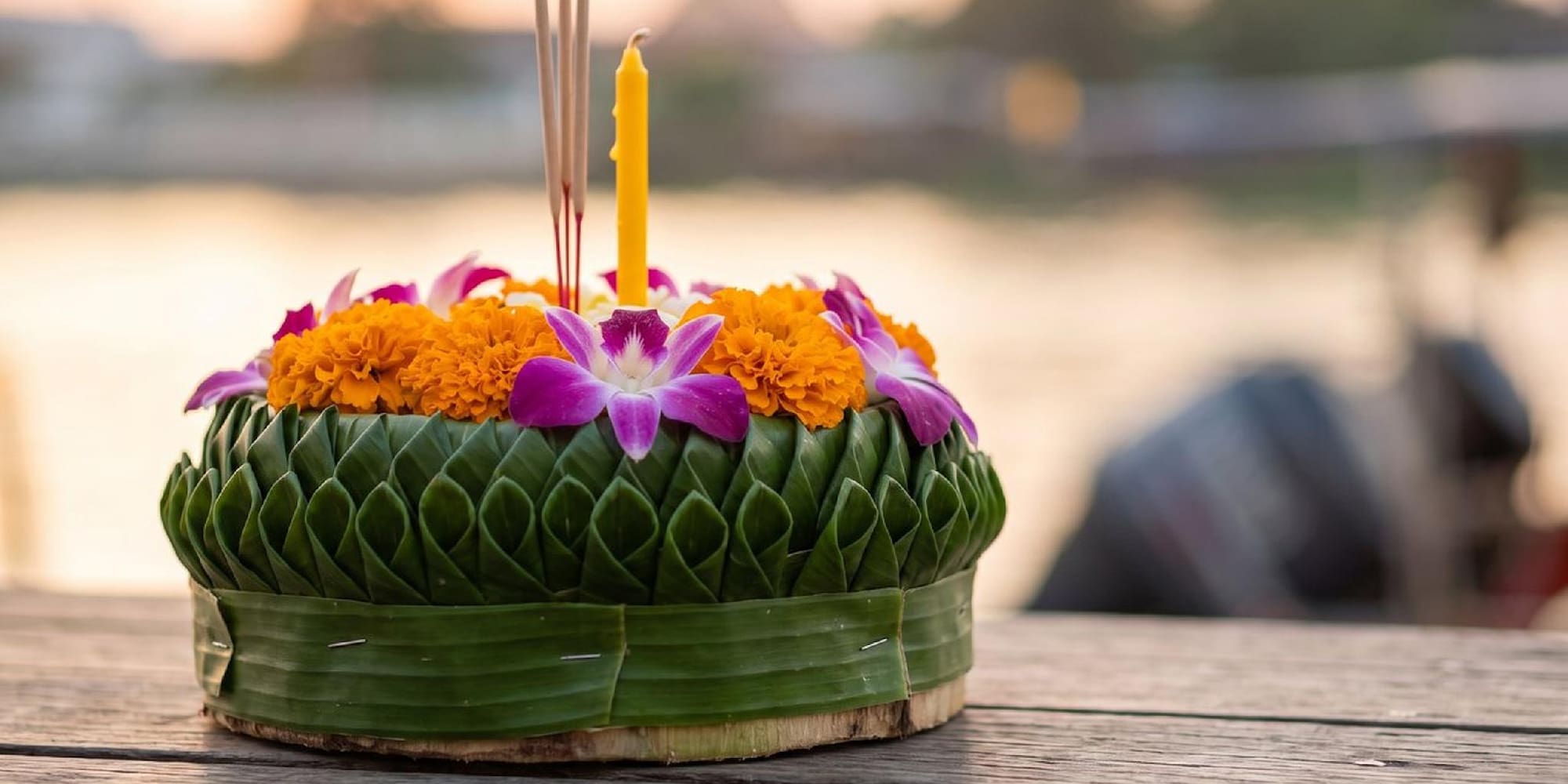 Thai Krathong offering: banana leaf, marigolds, orchids, candle, incense on wood.