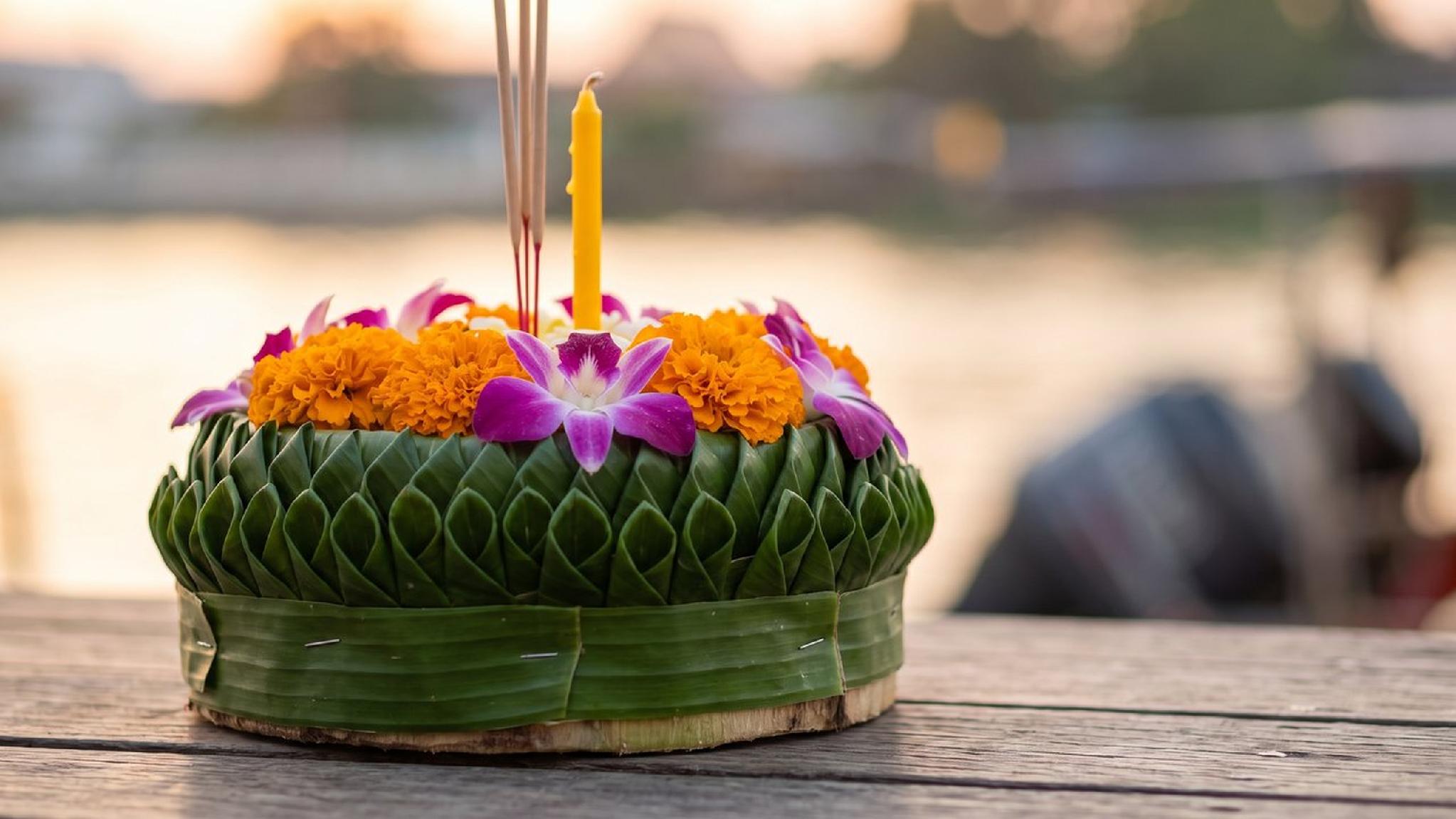 Thai Krathong offering: banana leaf, marigolds, orchids, candle, incense on wood.