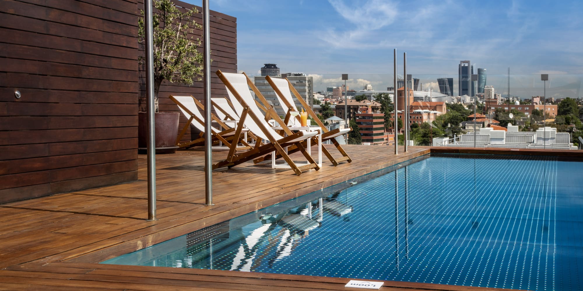 Rooftop pool deck with lounge chairs overlooking Madrid city skyline.