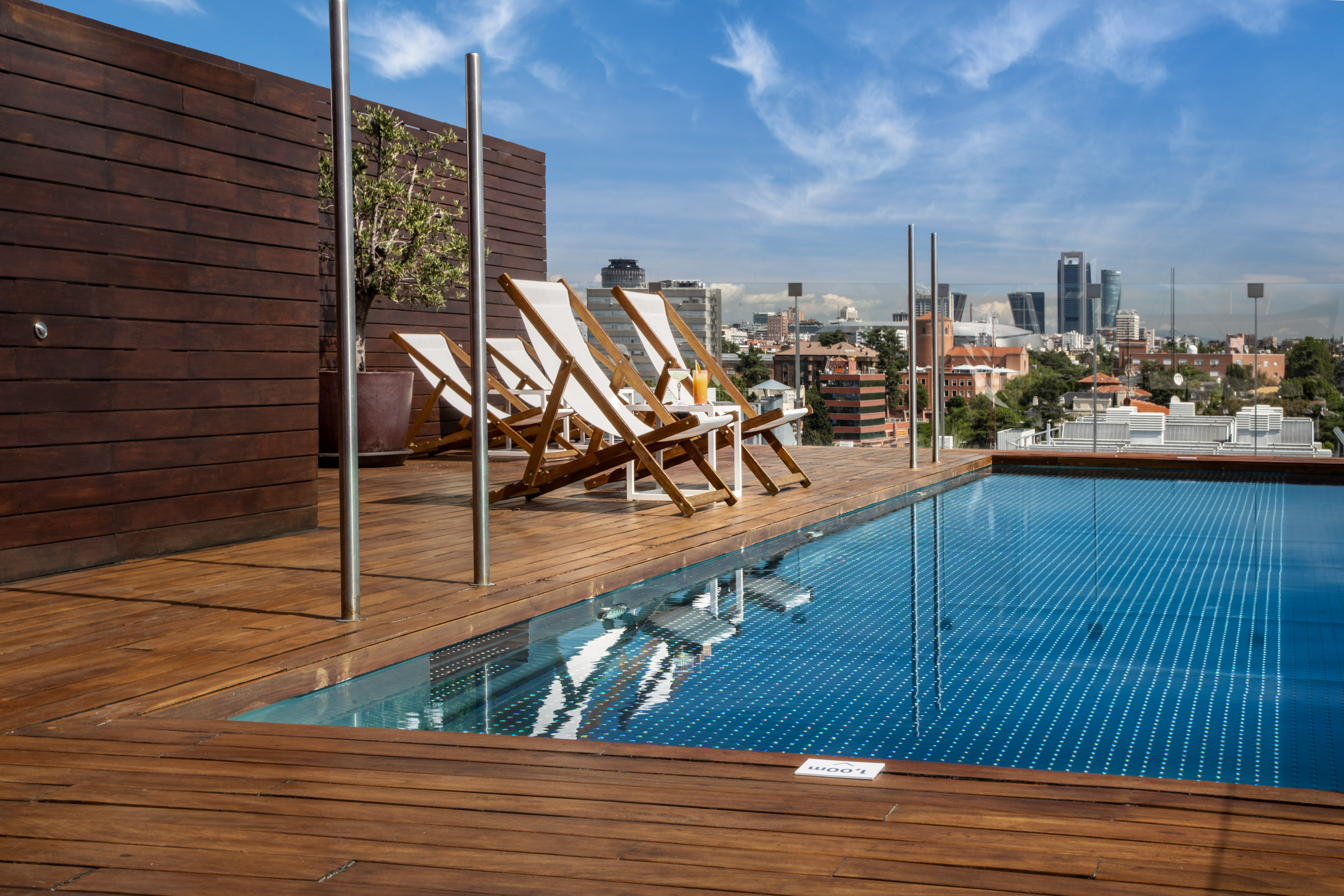 Rooftop pool deck with lounge chairs overlooking Madrid city skyline.