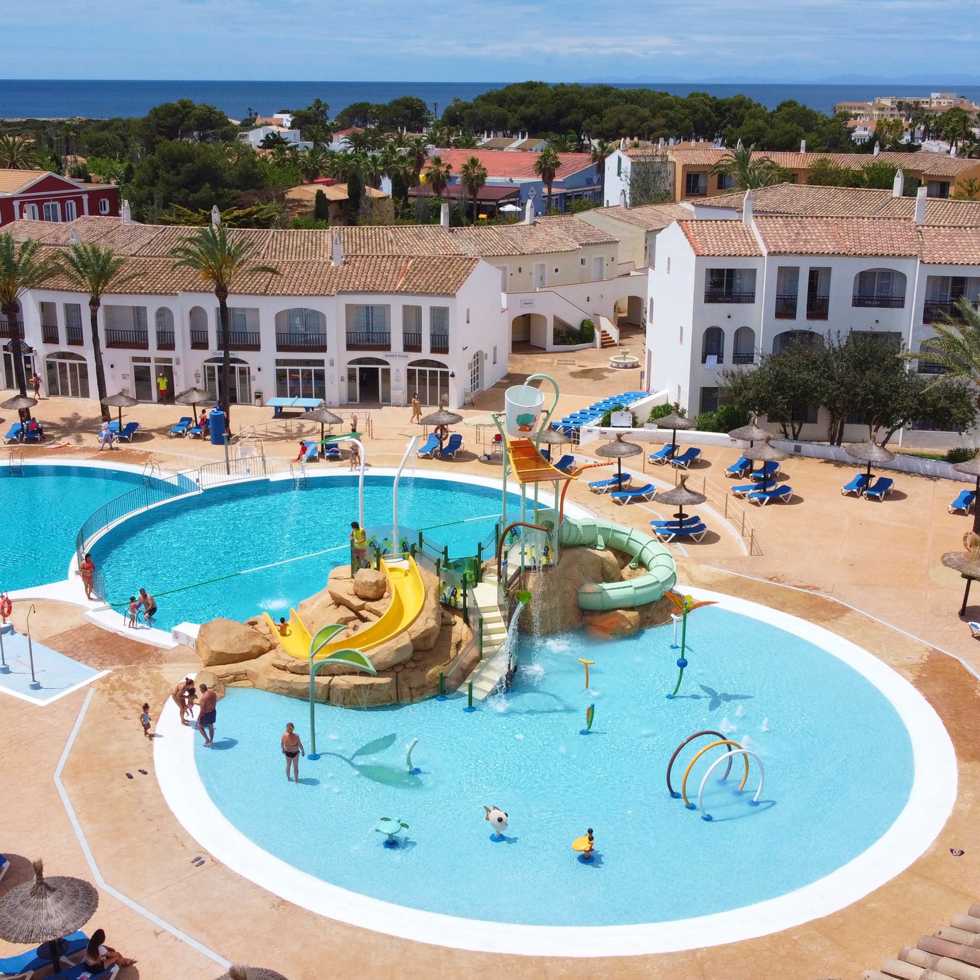 Mediterranean resort pools, water park, palm trees, and distant ocean view.
