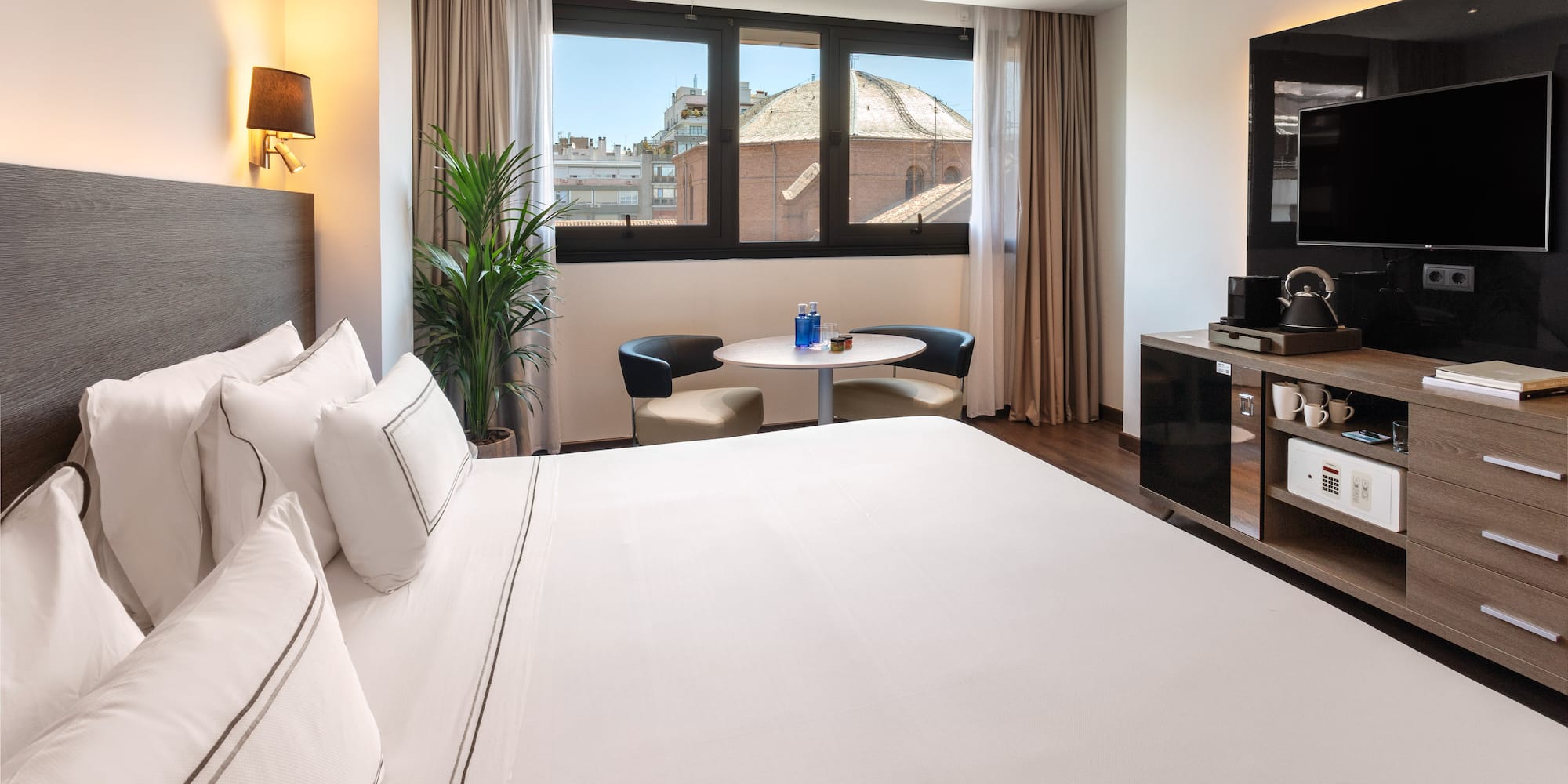 Modern hotel room with comfortable bed, city view window, and minibar.