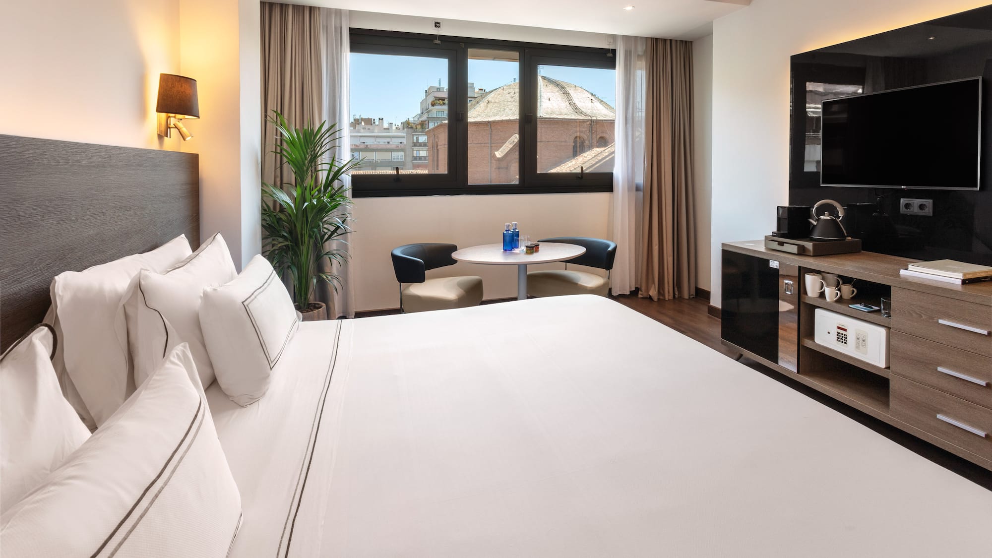 Modern hotel room with comfortable bed, city view window, and minibar.