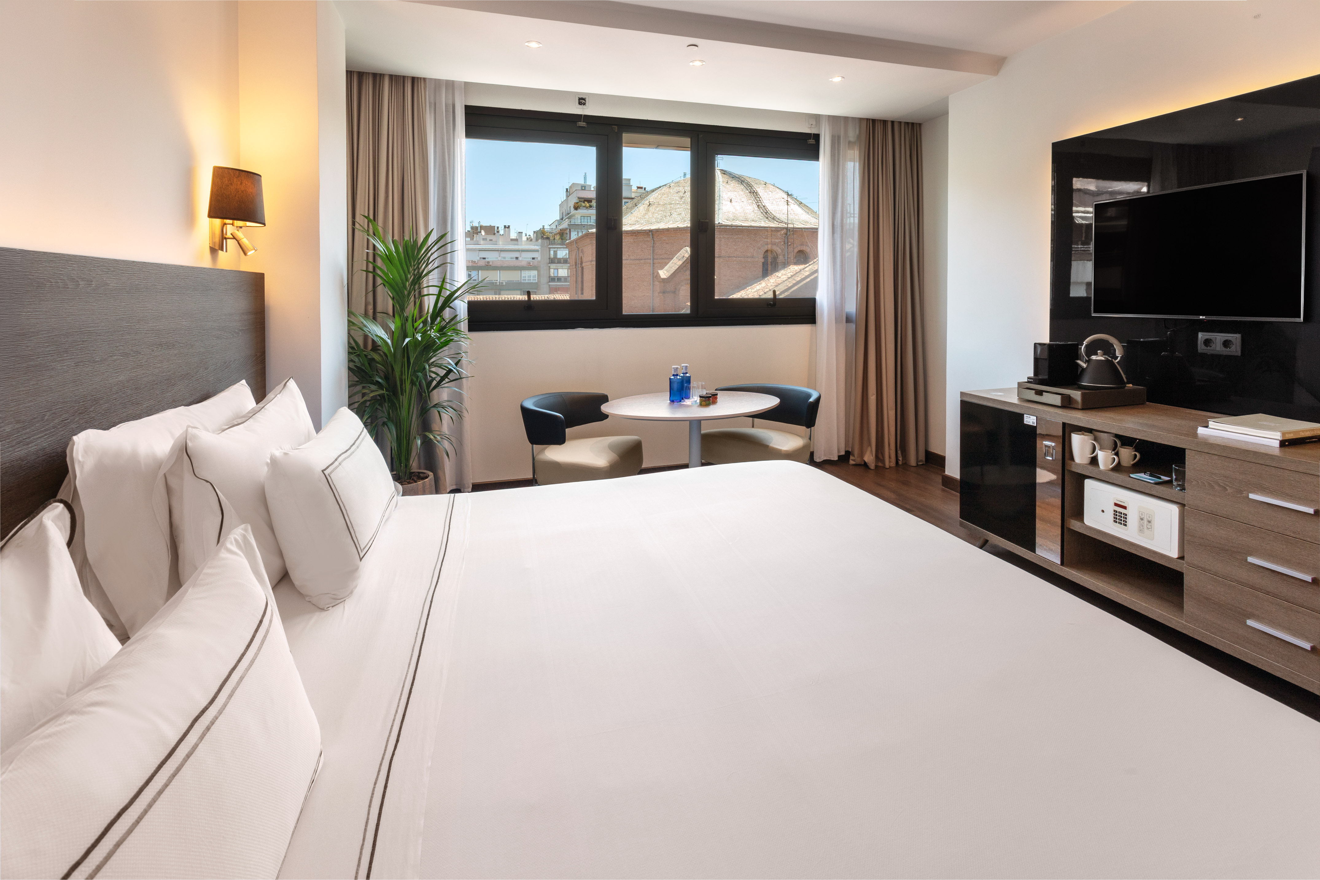 Modern hotel room with comfortable bed, city view window, and minibar.