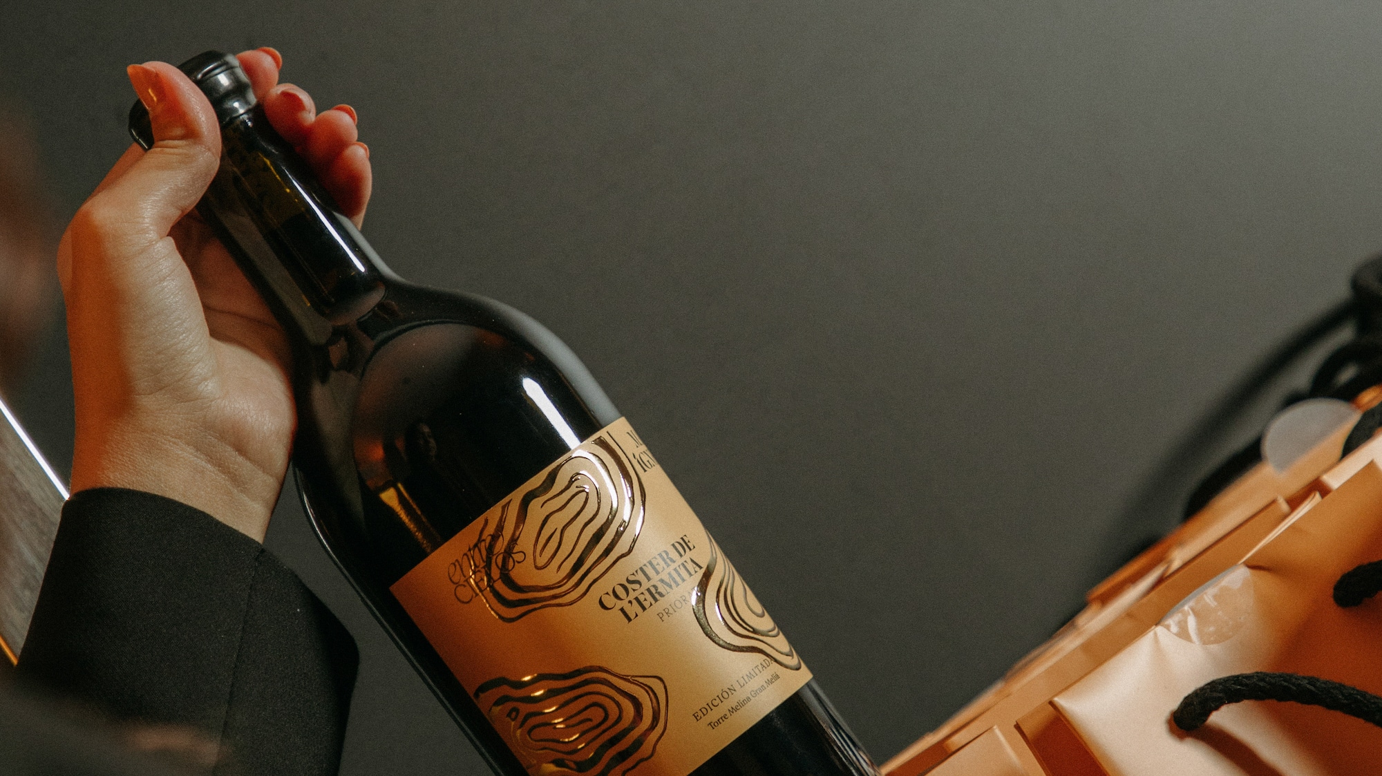 Hand holding Coster de l'Ermita Priorat red wine bottle in orange gift bag.