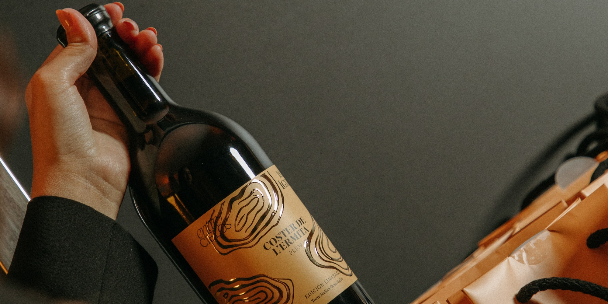 Hand holding Coster de l'Ermita Priorat red wine bottle in orange gift bag.