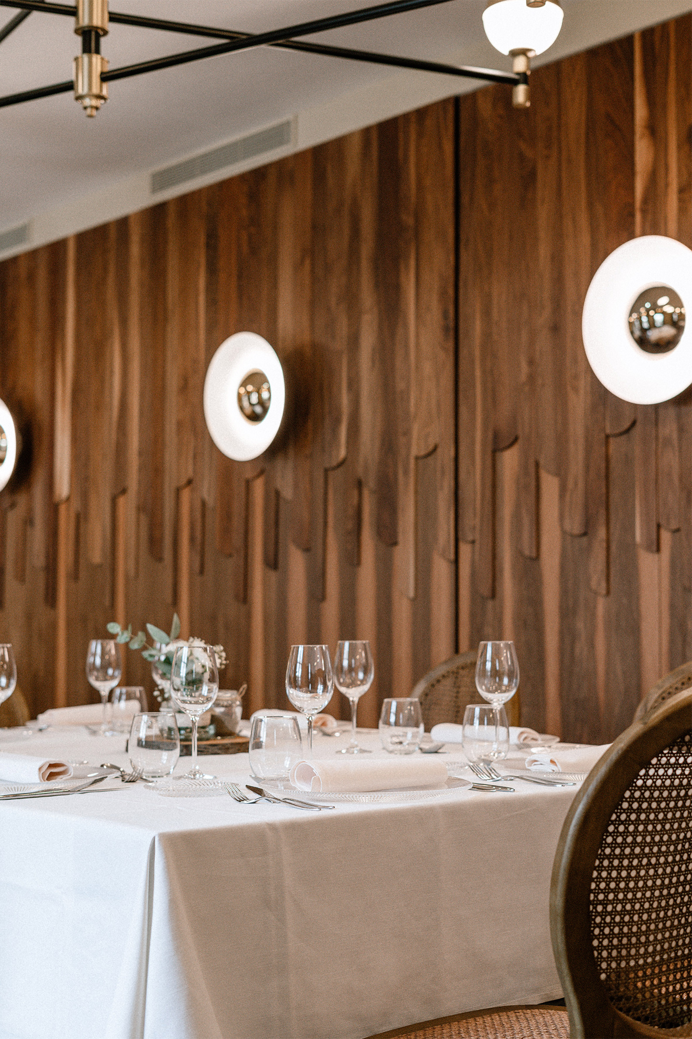 Restaurant dining table with white cloth, glassware, modern lighting, wooden wall. - Salón Espolita - Palacio de Avilés Afiliat Meliá, Avilés
