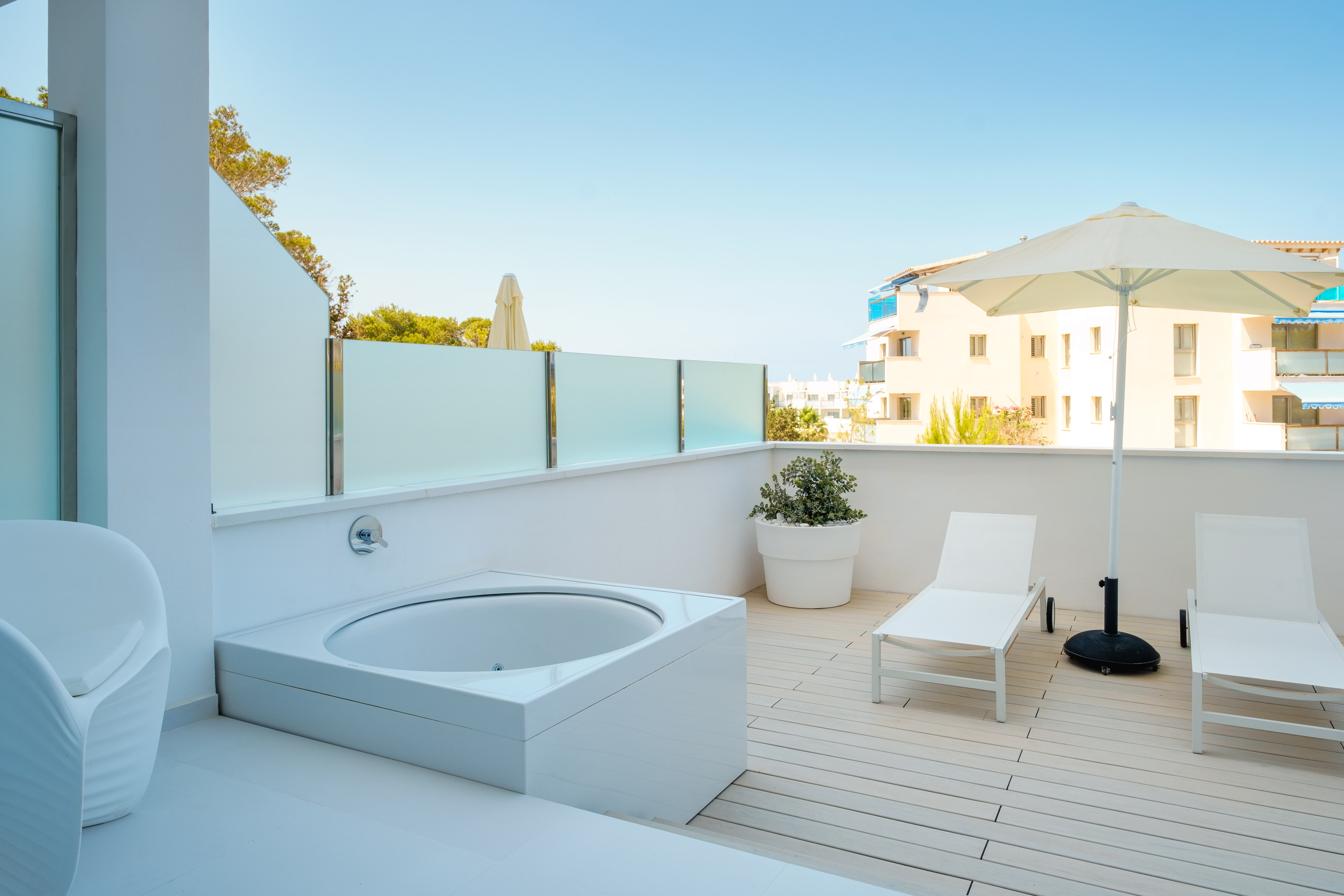 Outdoor hot tub on a modern white terrace with sun loungers.