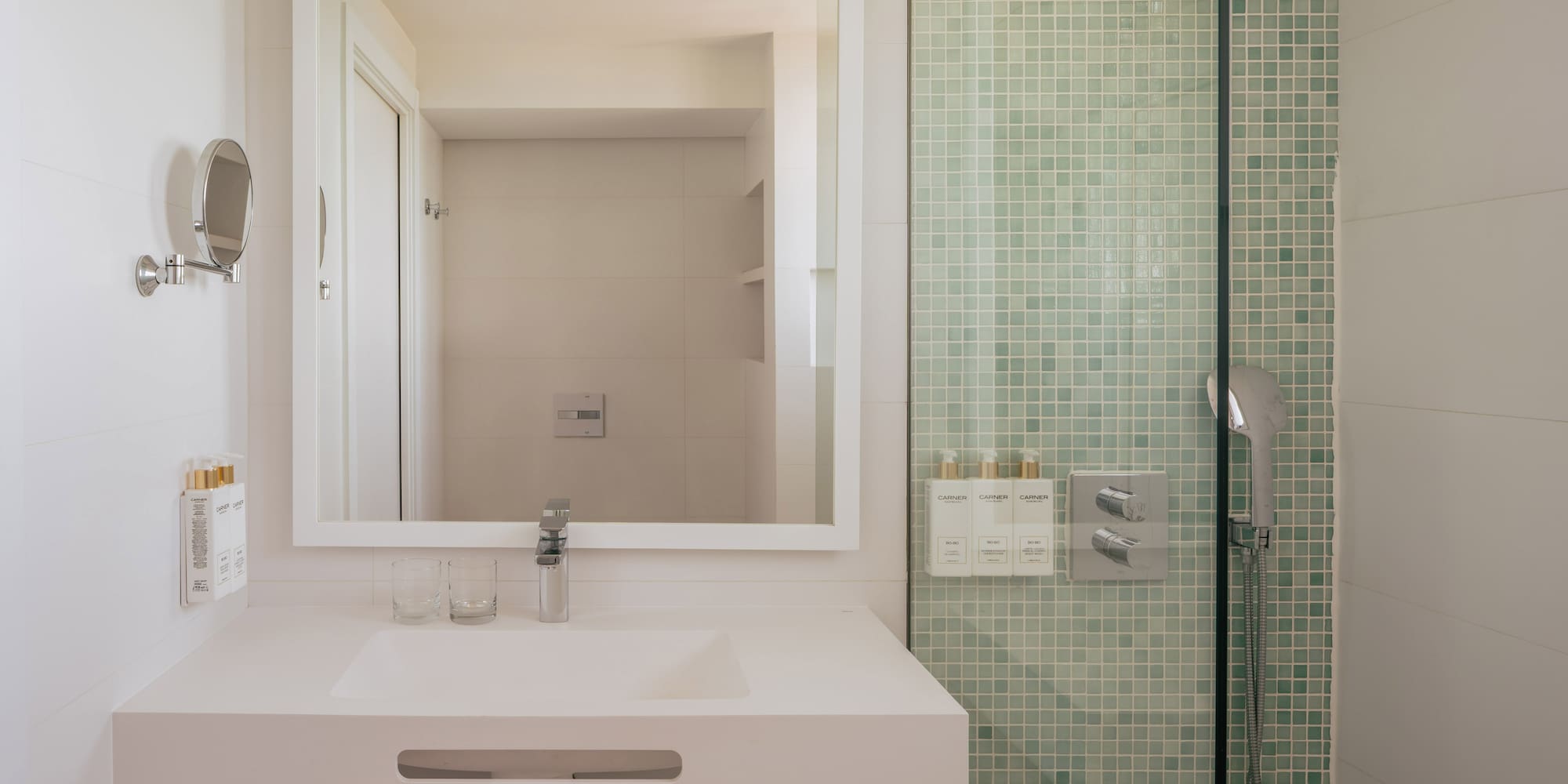 Modern hotel bathroom vanity with mirror and green mosaic tile shower.