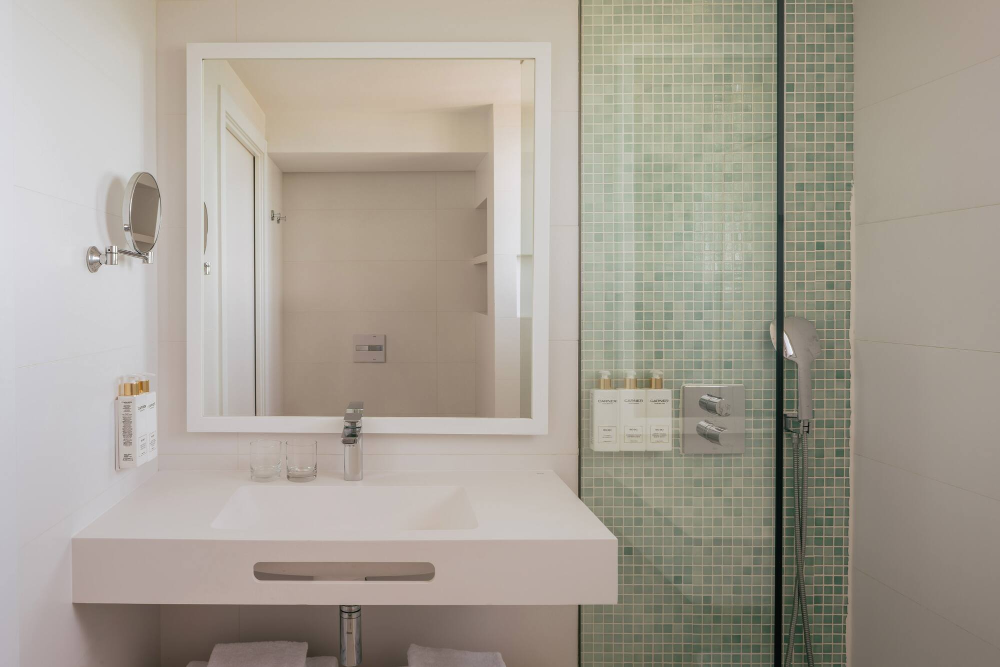 Baño moderno, lavabo blanco, espejo, ducha con azulejos verdes menta.
