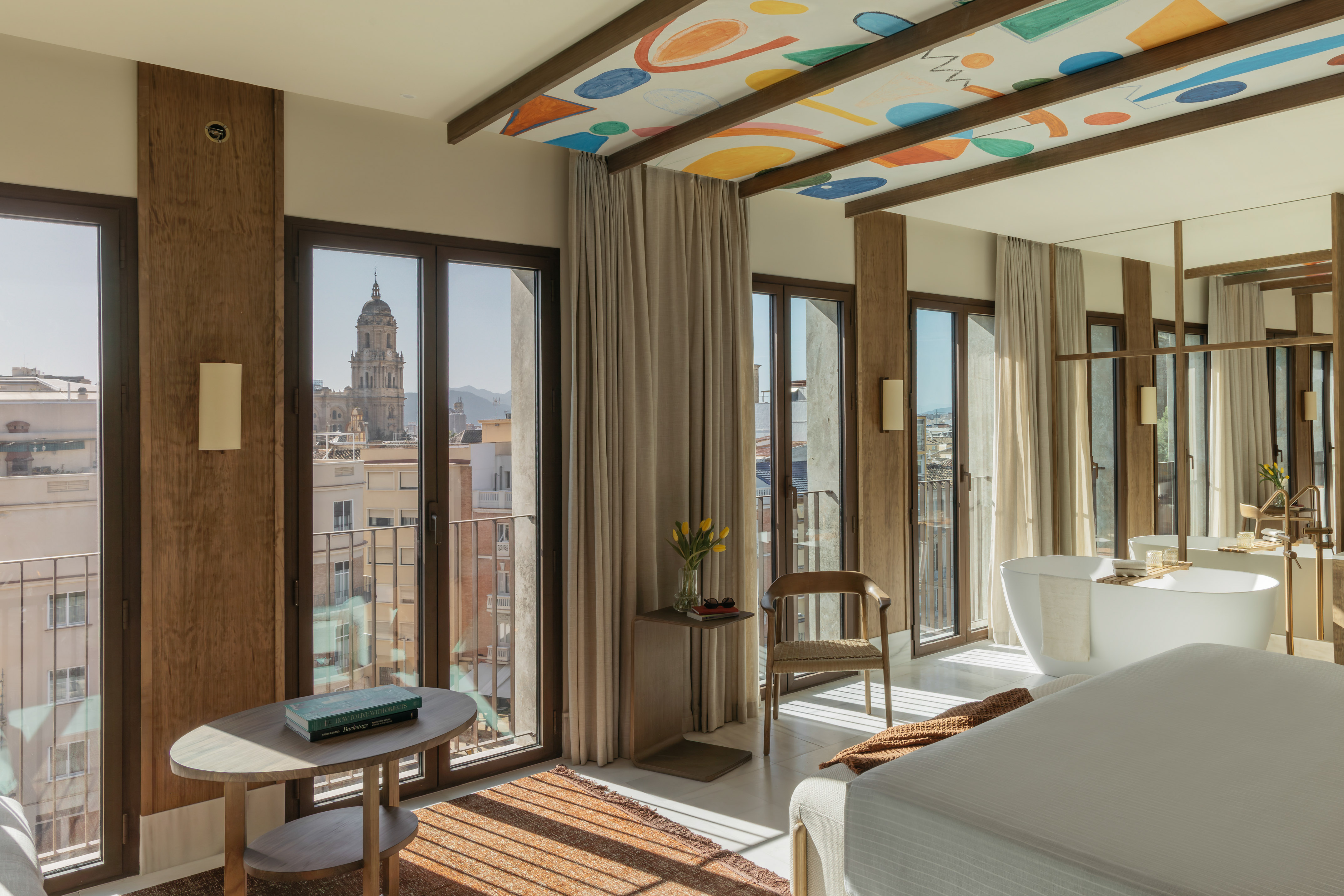 Modern Malaga hotel suite with cathedral view, colorful ceiling, and bathtub.
