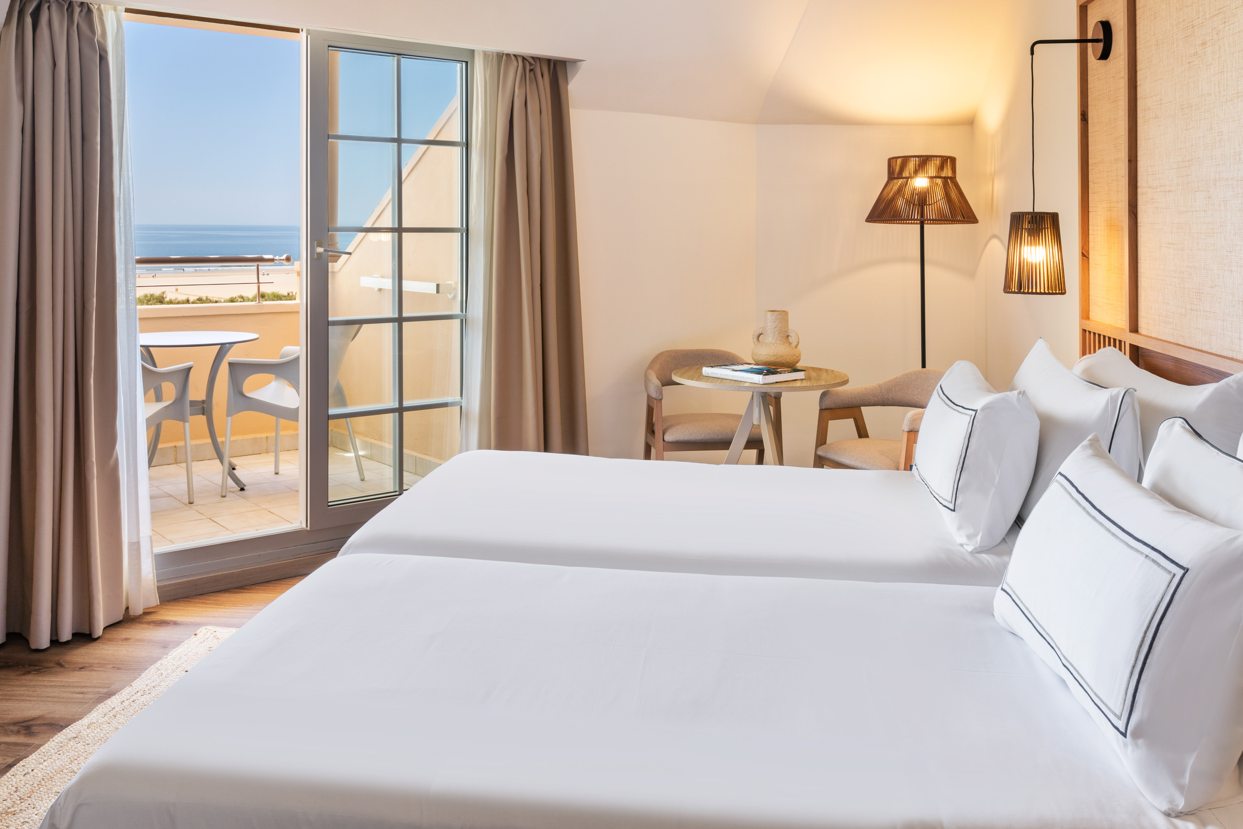 Hotel room with twin beds and a balcony offering sea and beach views.