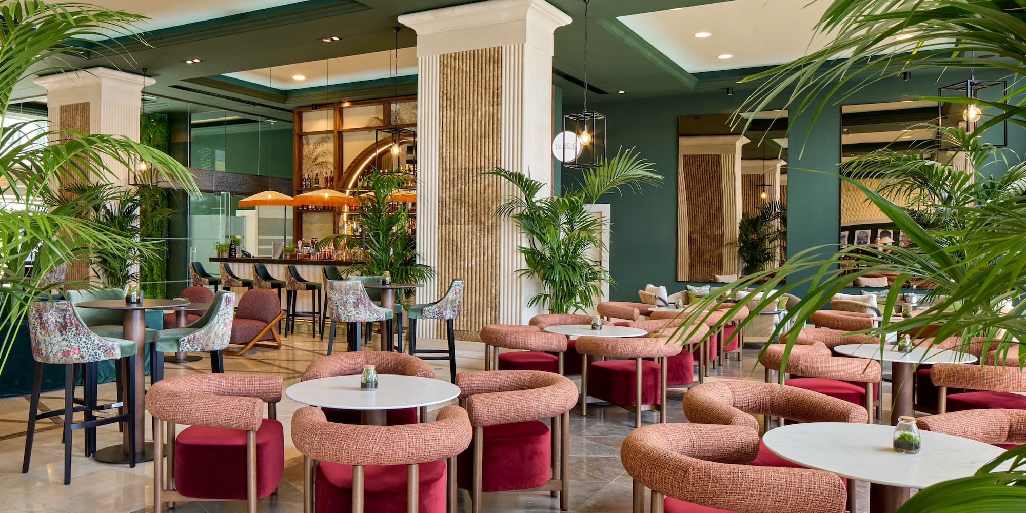 Contemporary hotel bar lounge with green walls, palm plants, and stylish red seating.