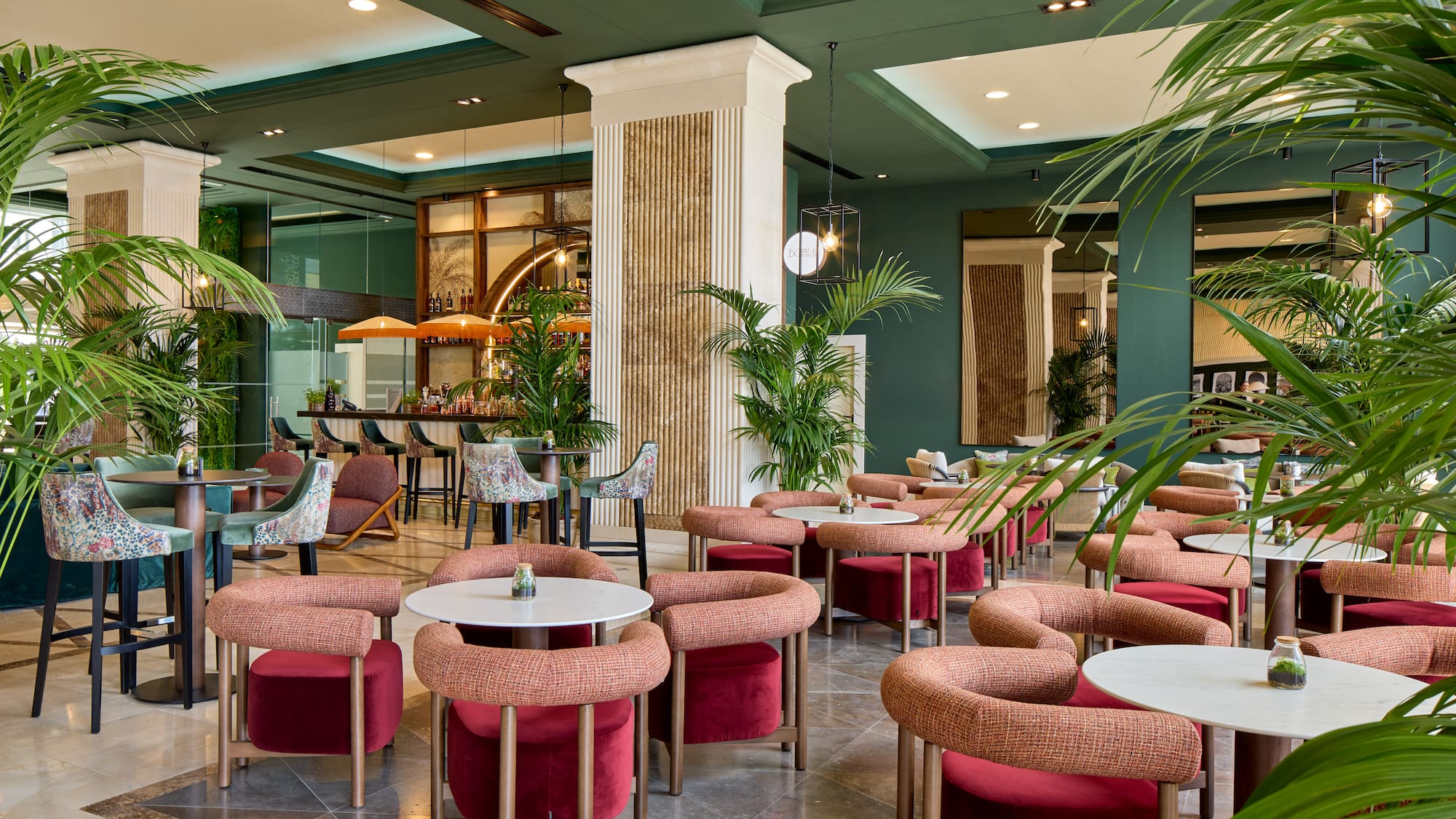 Modern hotel bar lounge with green decor, palm plants, and vibrant seating.