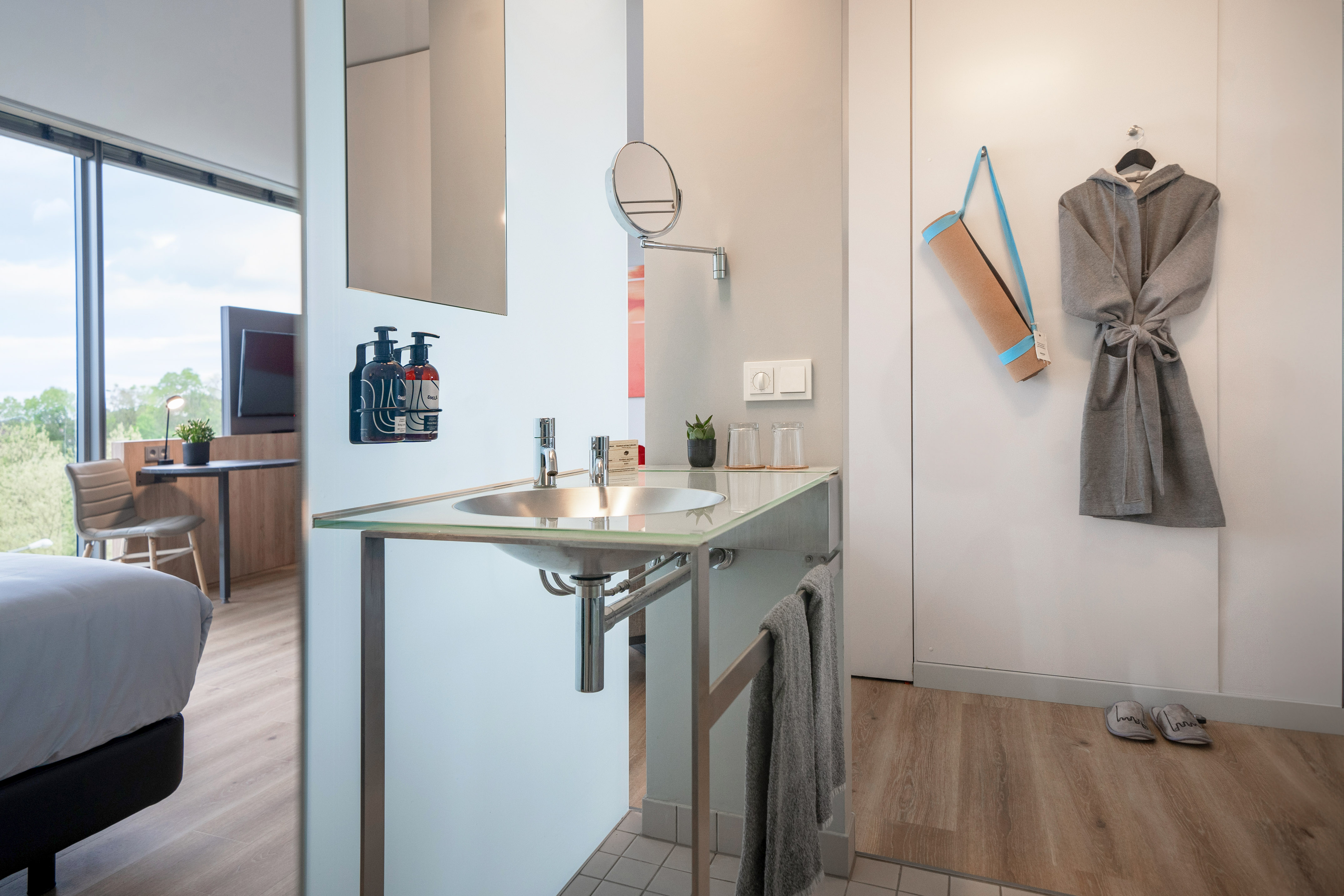 Modern hotel room with bathroom vanity, mirror, yoga mat, and bathrobe.