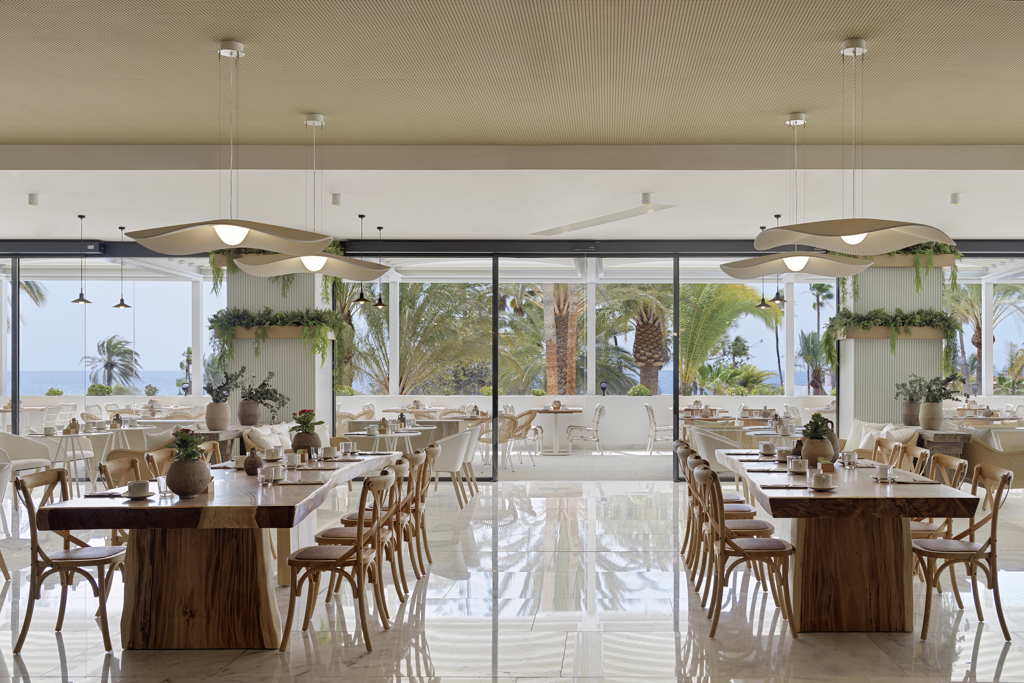 Modern beachfront restaurant with sea view, palm trees, and wooden tables.