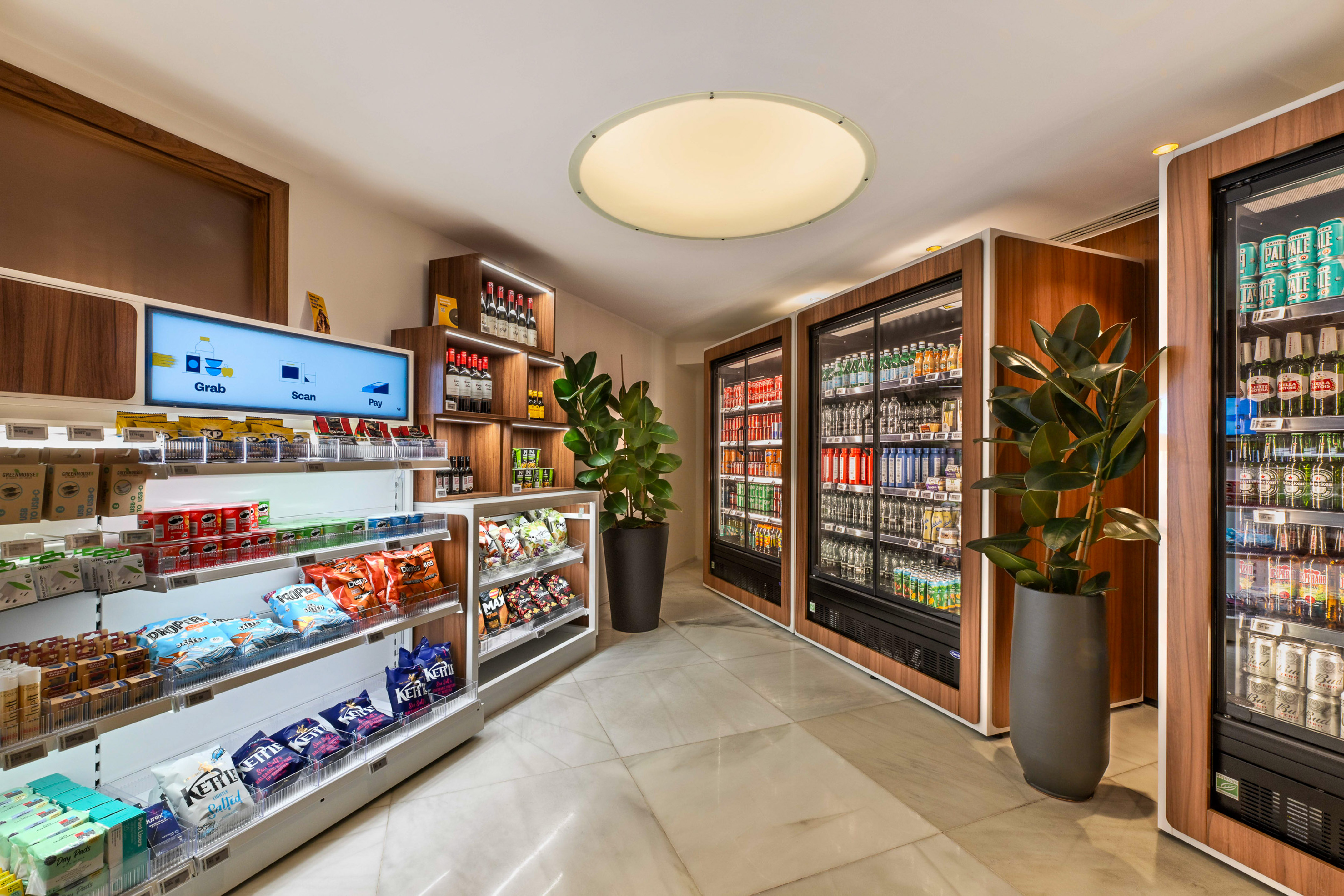 Automated grab-and-go store with shelves of snacks, beverages, and a self-checkout screen.