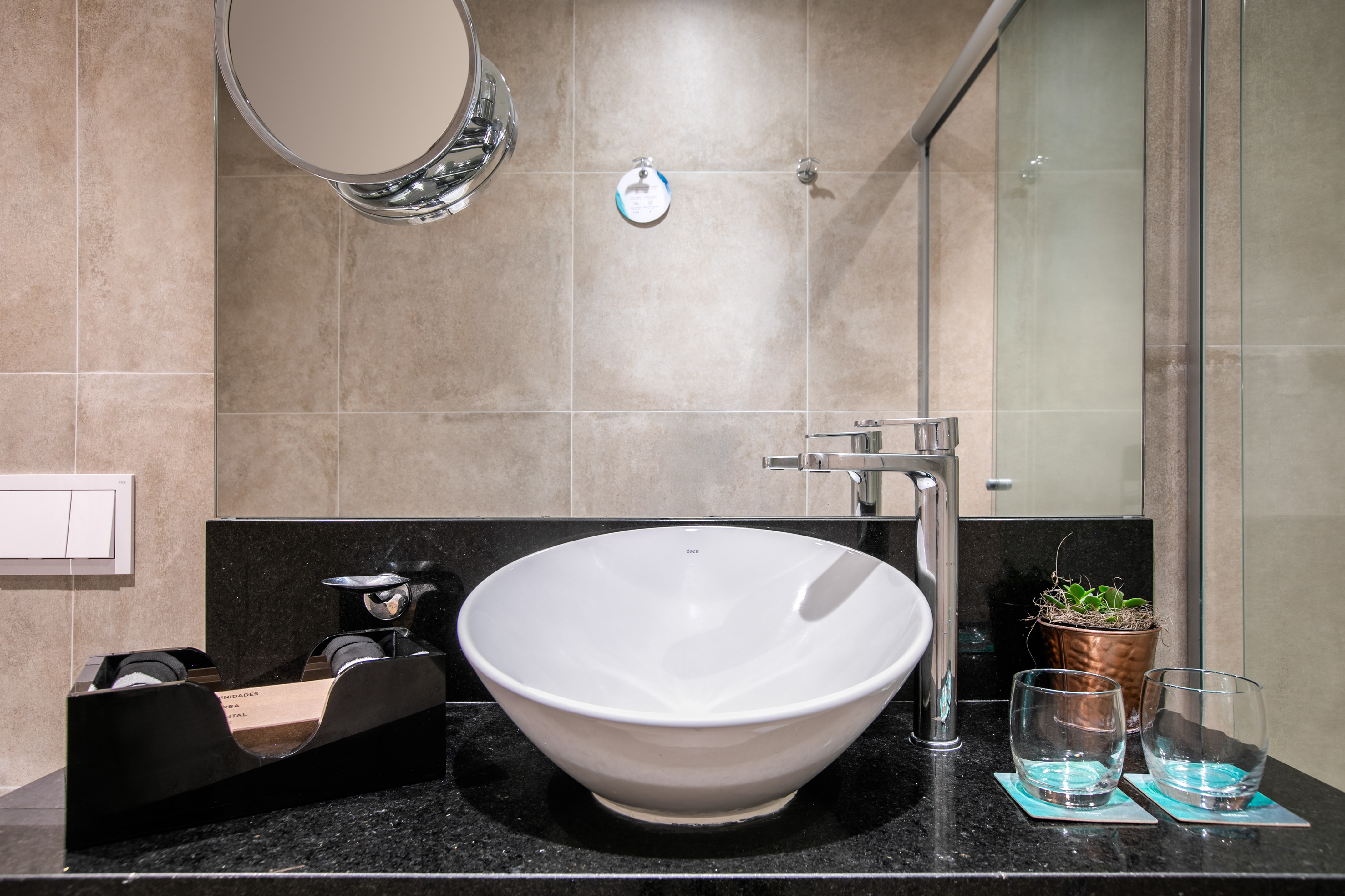 Modern hotel bathroom with white vessel sink, chrome faucet, and black counter.