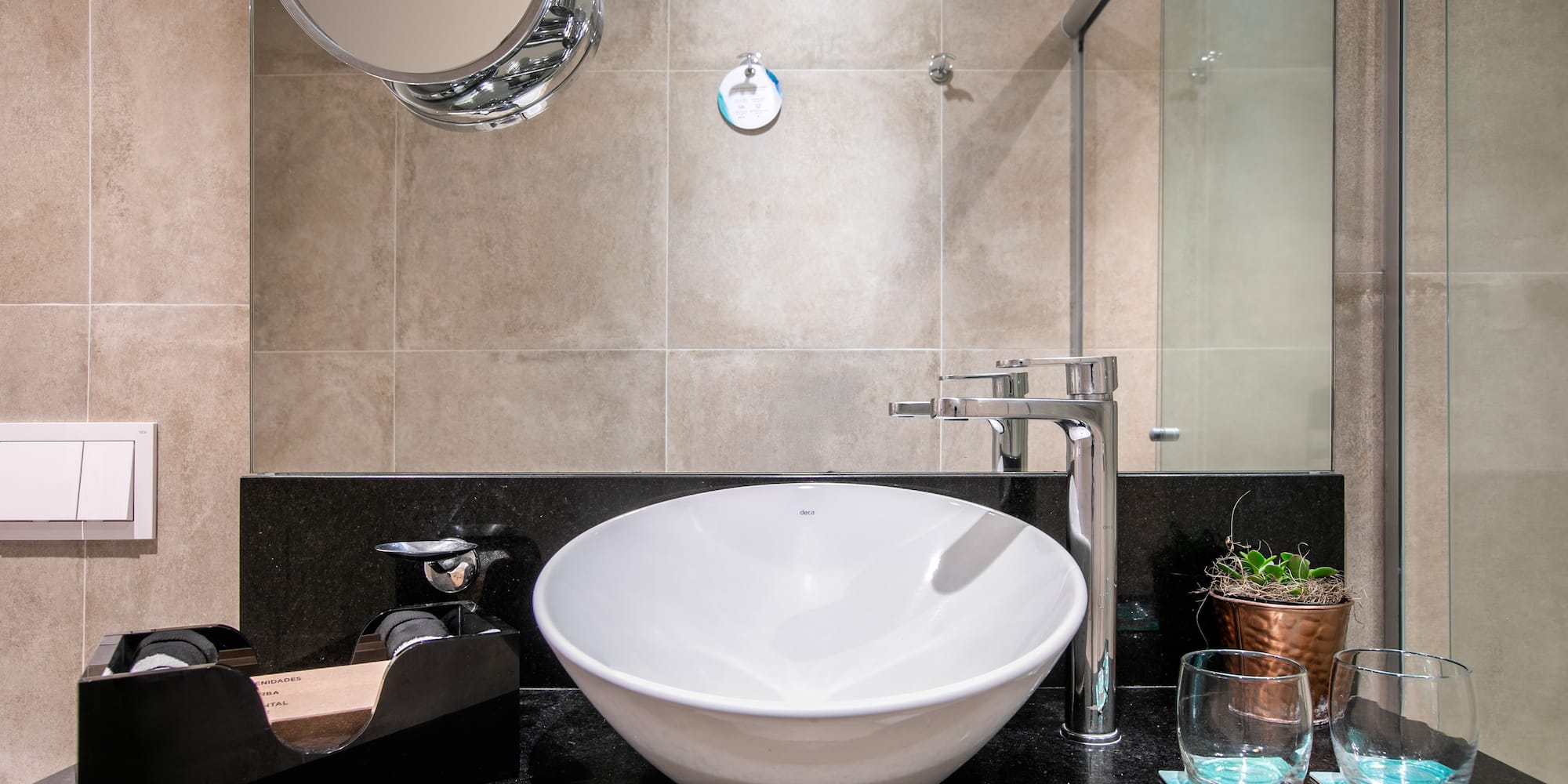 Modern hotel bathroom with white vessel sink, chrome faucet, and black counter.